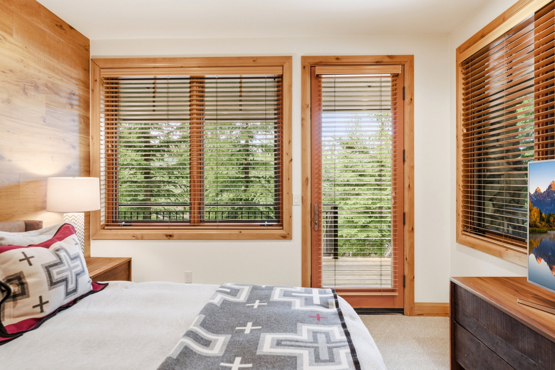 Bedroom featuring wood-finish accent wall, wood-trimmed windows with blinds, and a wood-trimmed door