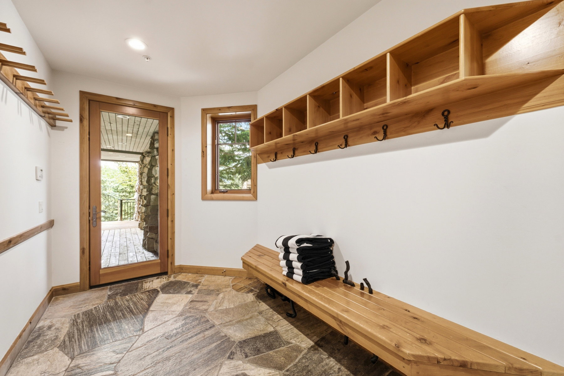 Entryway featuring natural stone-finish flooring, a full-lite wood-frame door, a built-in wood bench, and a built-in wood shelving unit with coat hooks