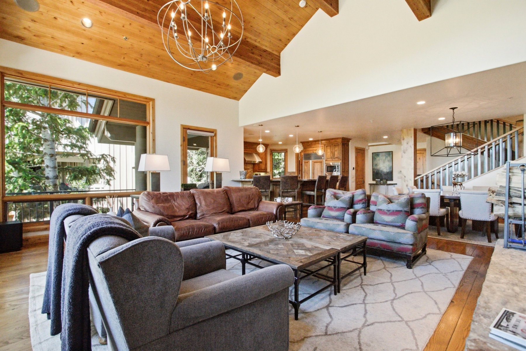 Spacious living area featuring a vaulted wood-paneled ceiling with exposed beams, wood-finish flooring, a contemporary chandelier, and large picture windows