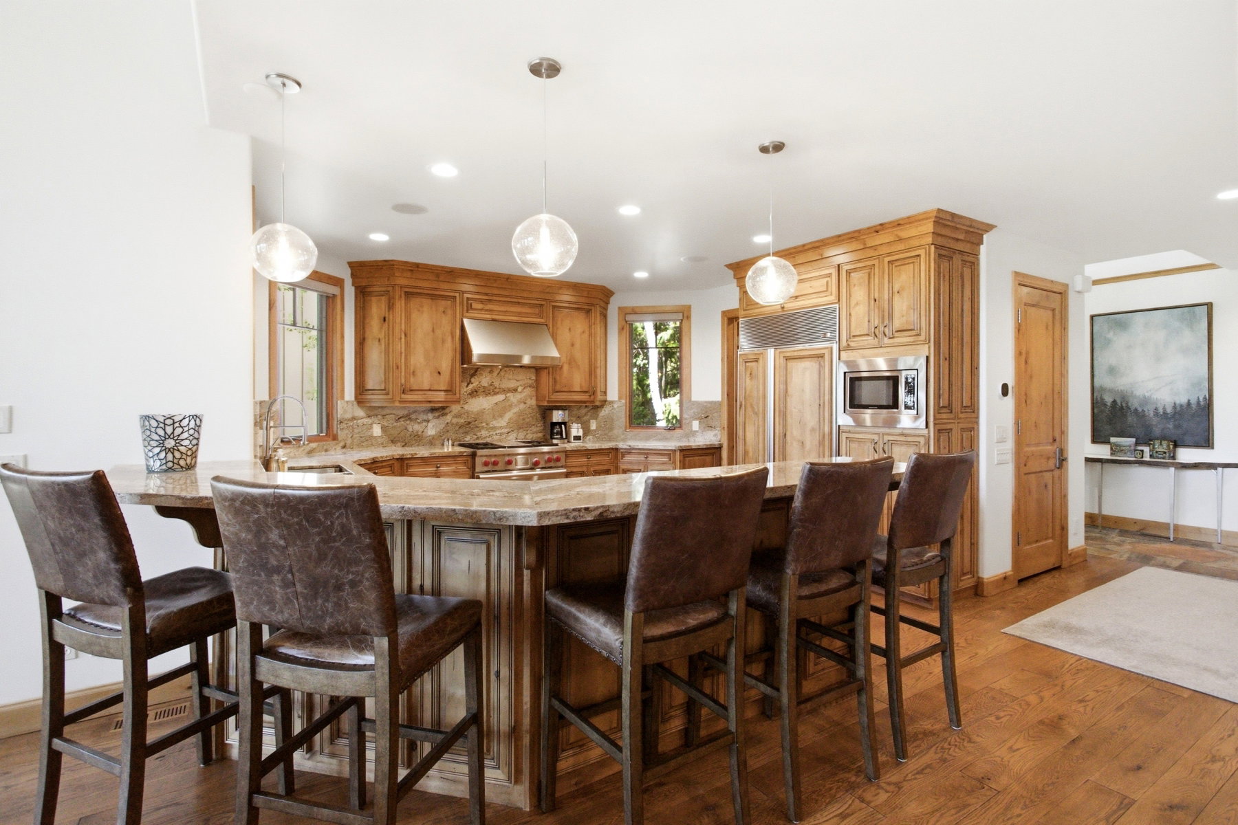 Gourmet kitchen featuring a substantial island with seating, natural wood cabinetry, integrated stainless steel appliances, and stone countertops