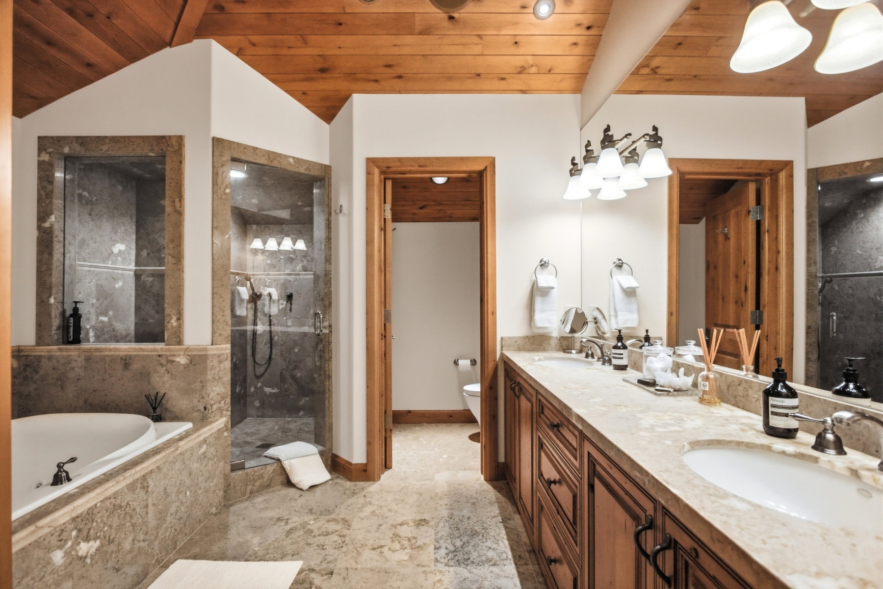 Bathroom featuring a dual vanity with undermount sinks, a built-in soaking tub, a glass-enclosed shower, wood-finish cabinetry, and a wood-paneled ceiling