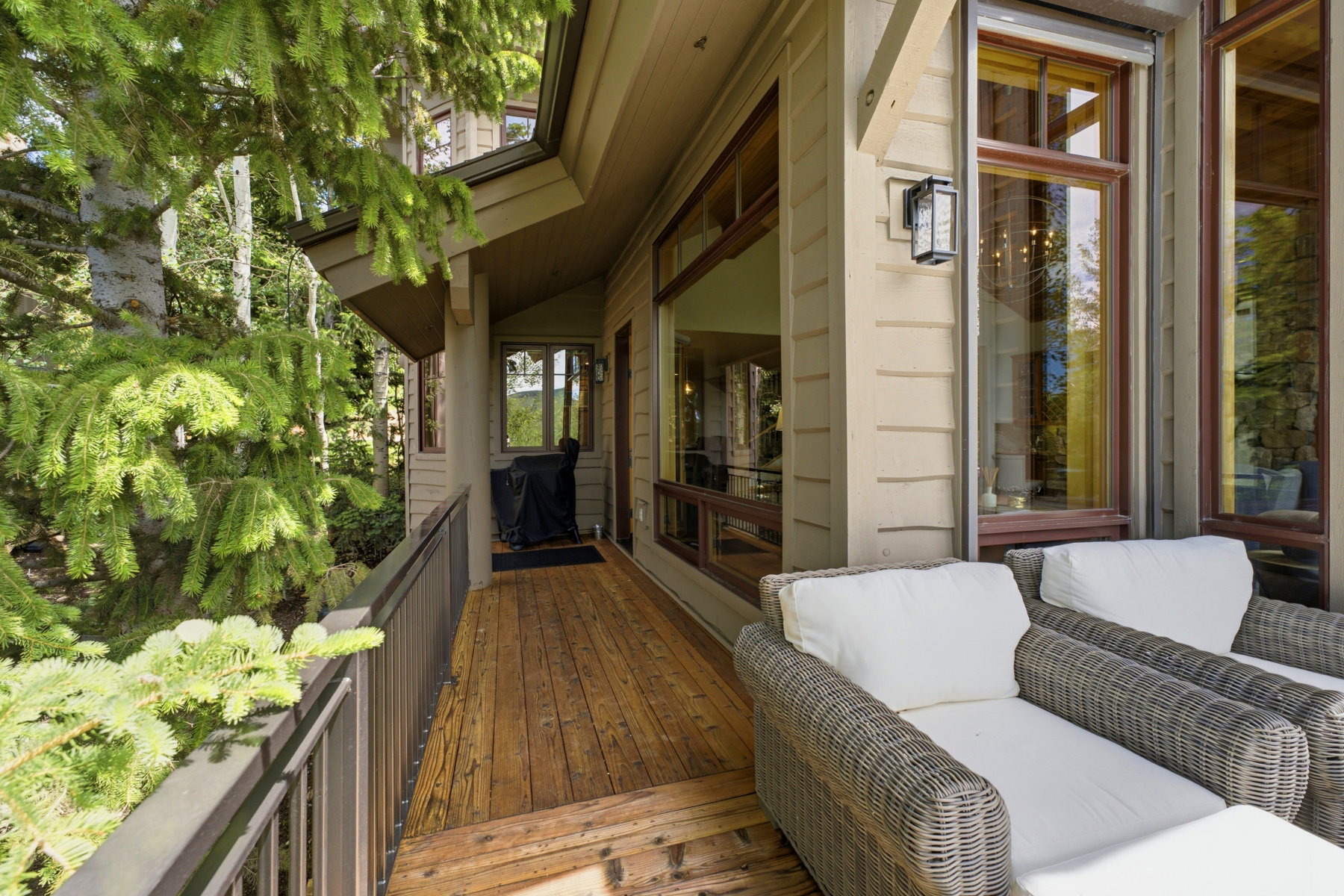 Wood-finish deck with a dark metal railing, featuring horizontal siding, large windows, and an outdoor wall sconce