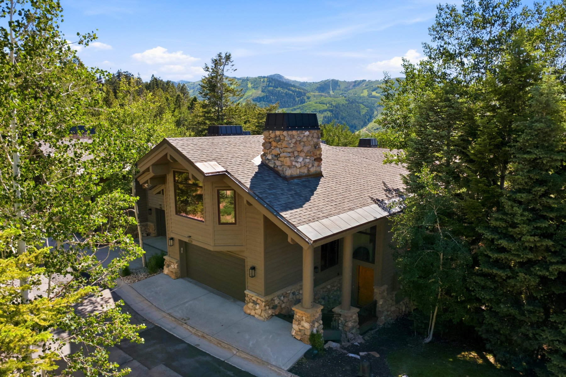Mountain-style residence featuring a stone chimney, stone accents, multiple large windows, and a two-car garage