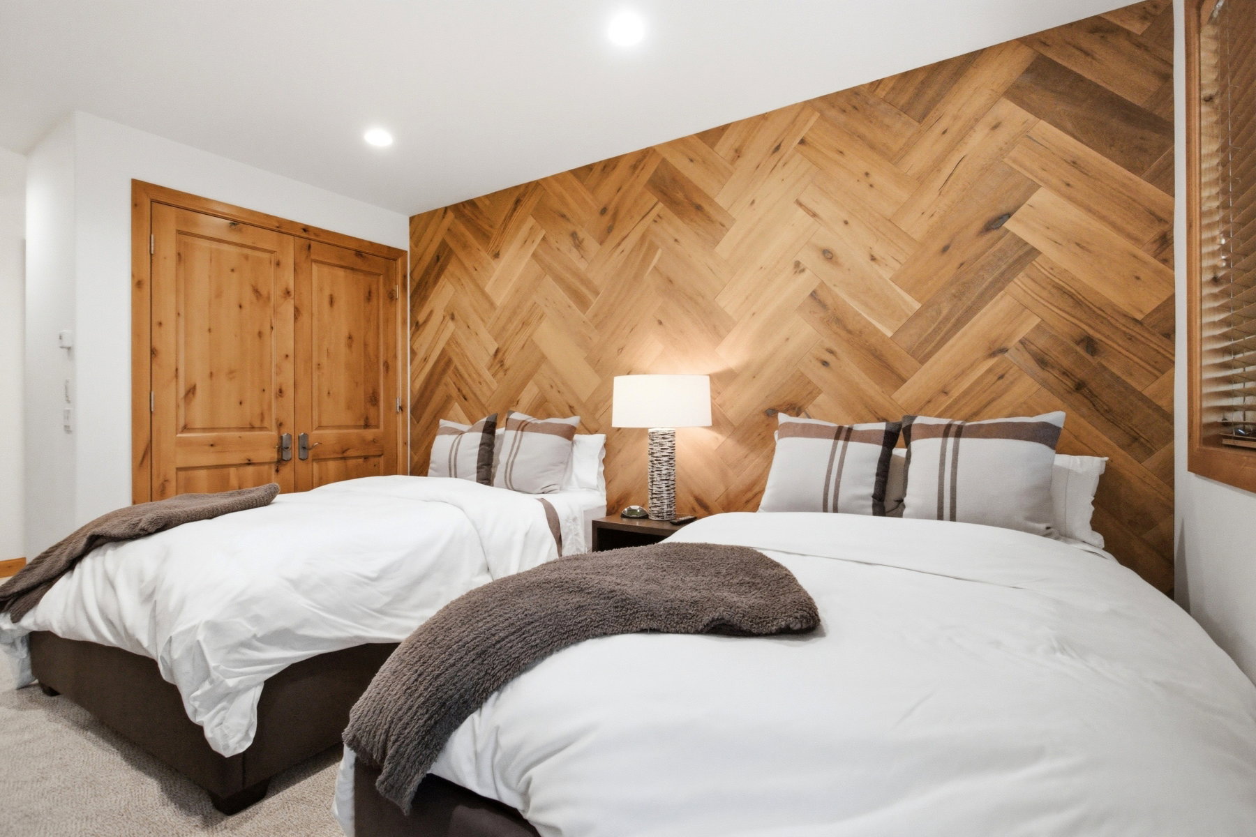 Bedroom featuring a herringbone wood-finish accent wall, twin beds with upholstered bases, recessed ceiling lighting, and natural wood bi-fold doors