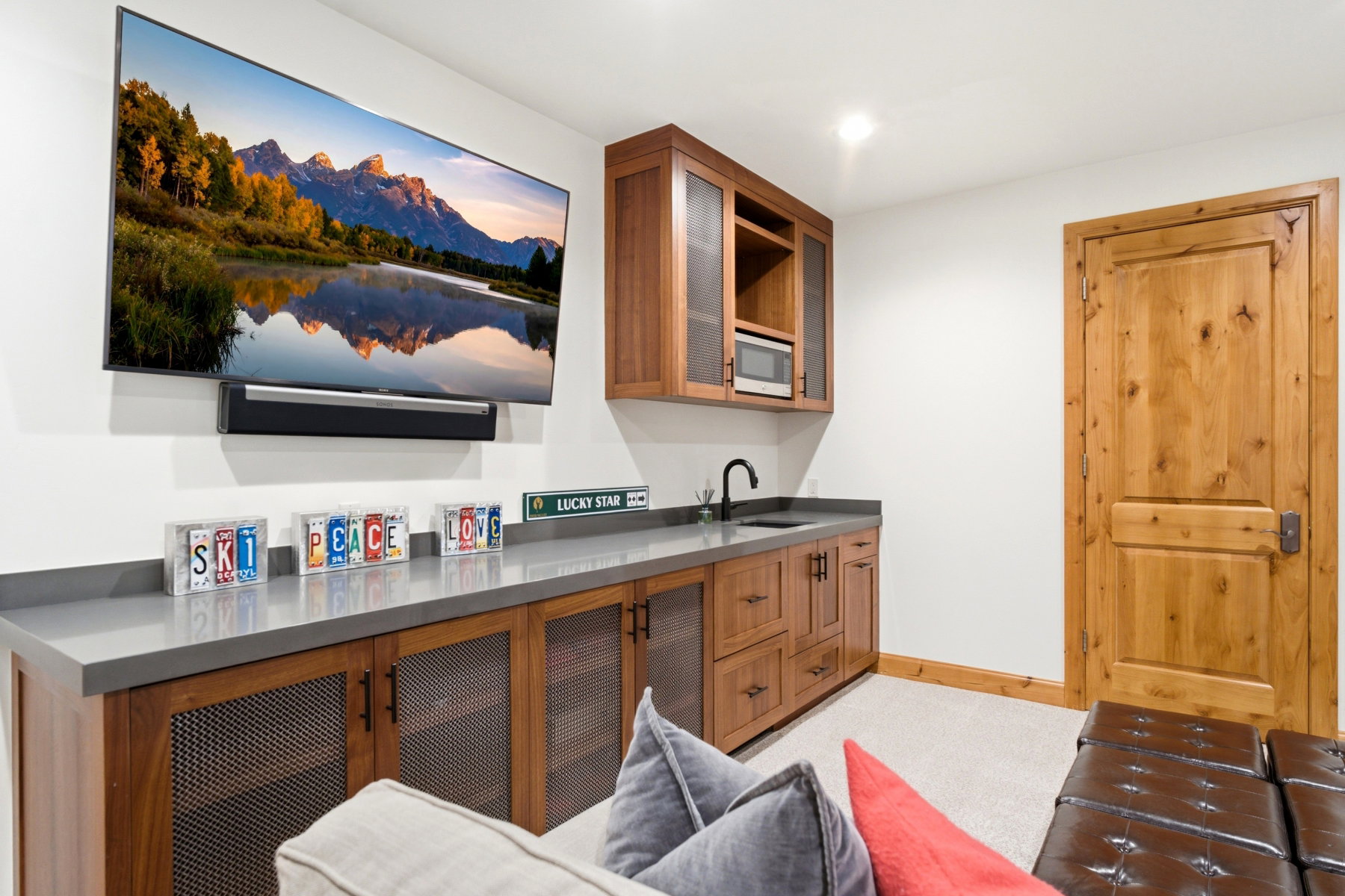 Entertainment area featuring a built-in wet bar with a black faucet and undermount sink, quartz countertops, and rich wood cabinetry with mesh paneling