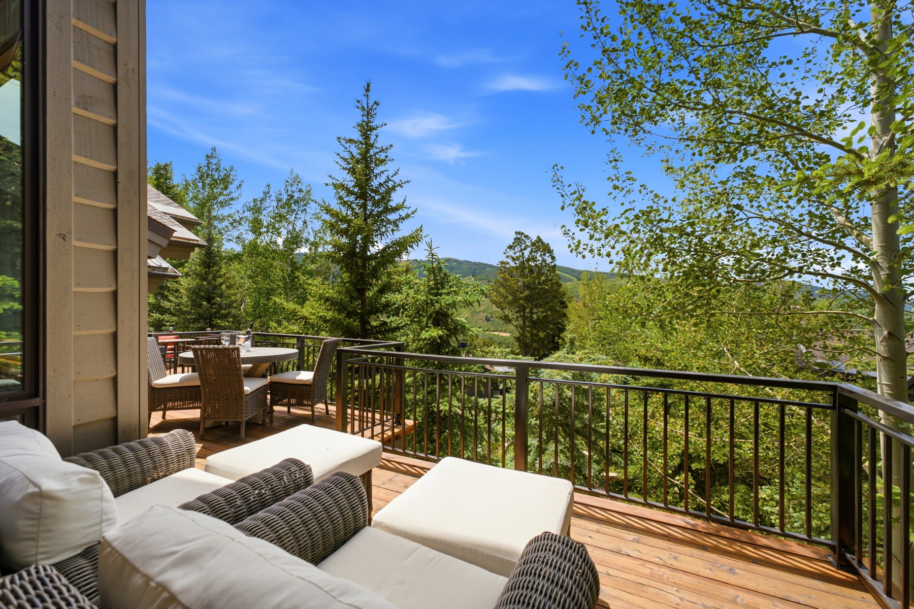 Expansive wood-decked balcony featuring a black metal railing and a forested mountainous backdrop