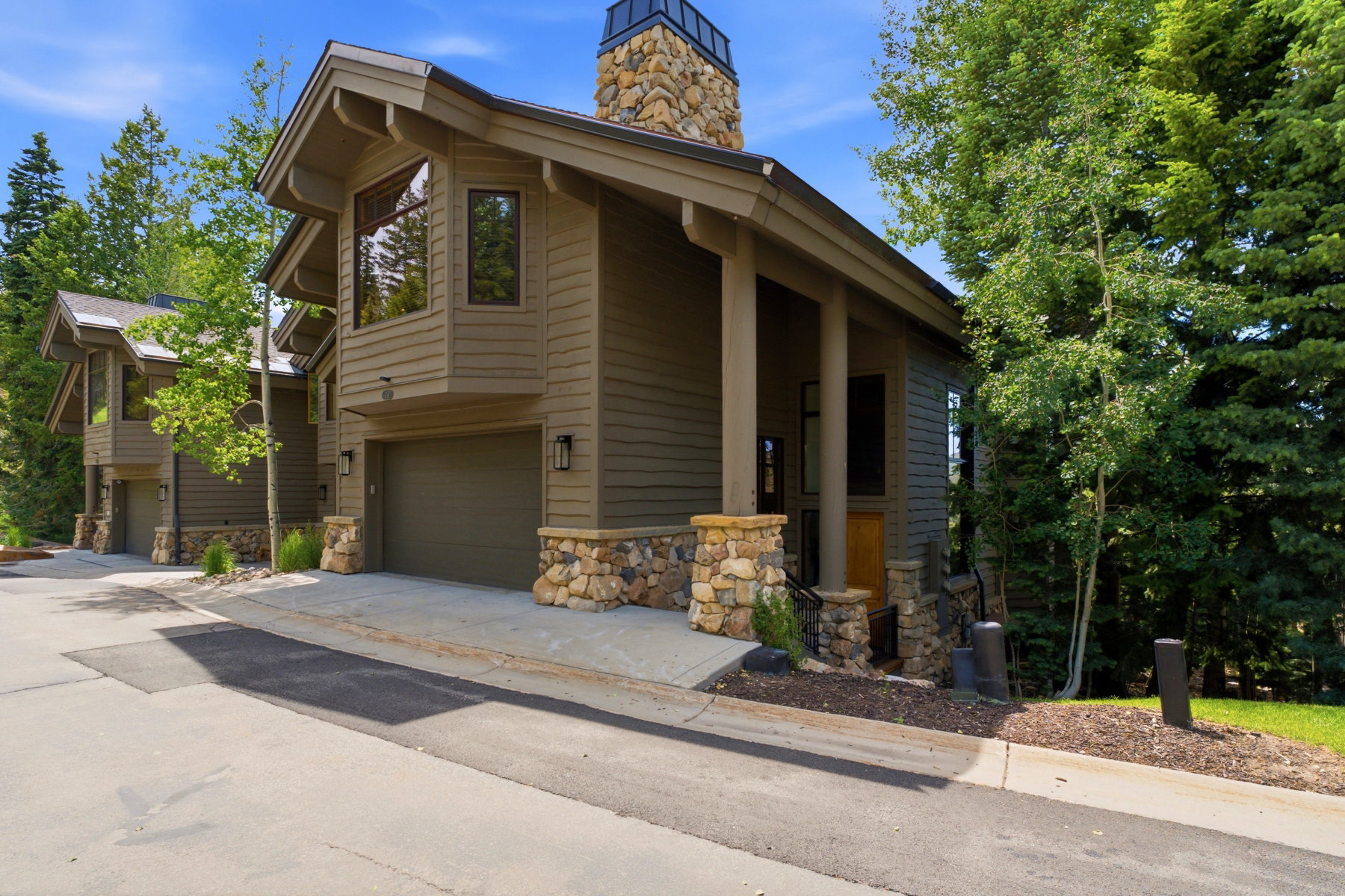 Modern alpine-style residence featuring siding, stone accents, an attached garage, and a prominent stone chimney