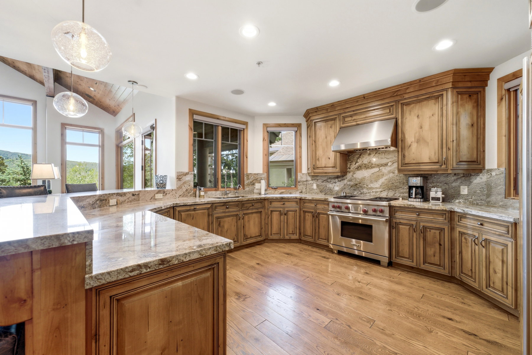 Gourmet kitchen featuring custom wood cabinetry, extensive stone countertops, a professional-grade stainless steel range, and wood-finish flooring