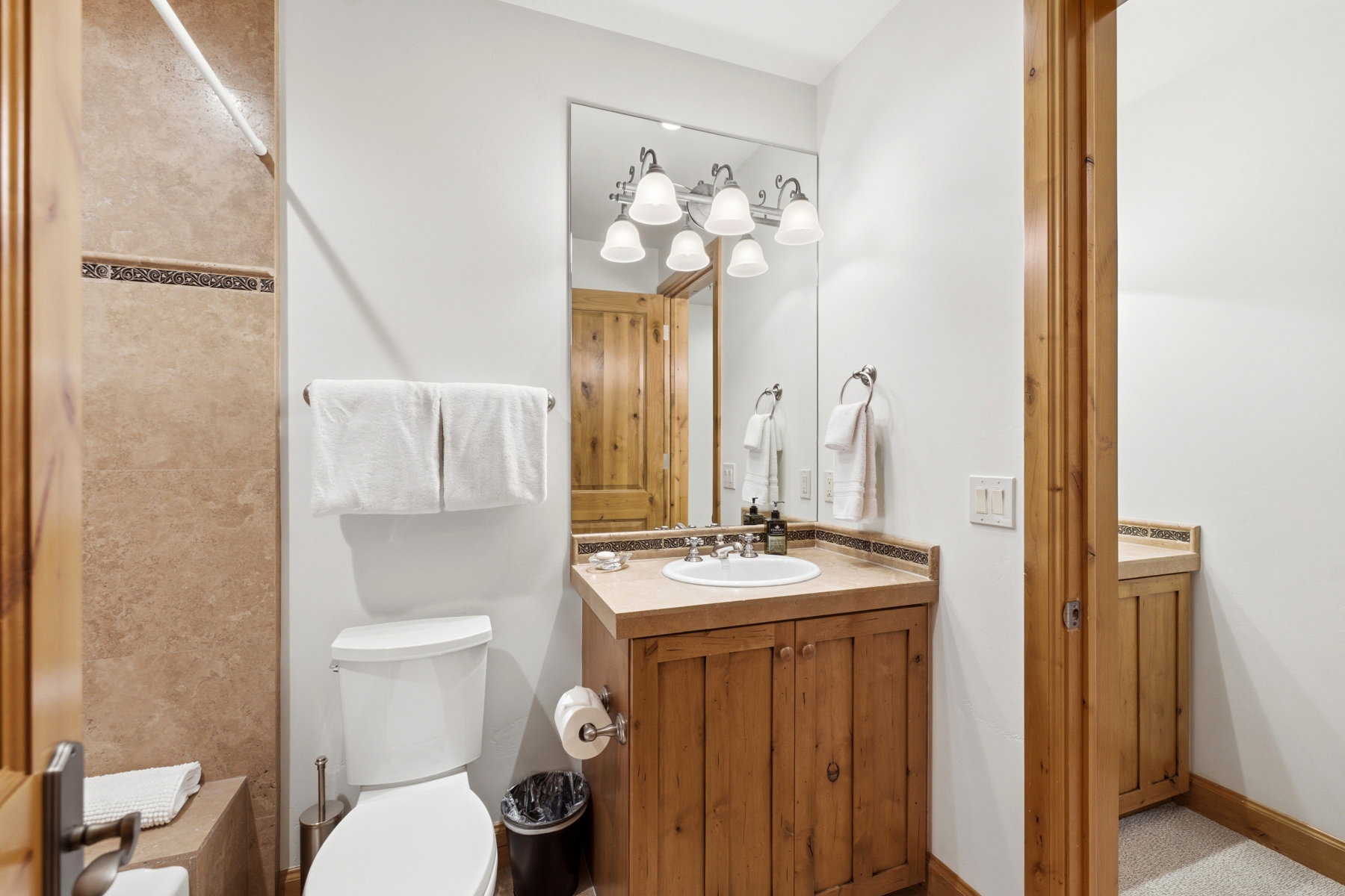 Bathroom featuring a wood-finish vanity with an integrated sink, a large wall-mounted mirror, and a five-light vanity fixture