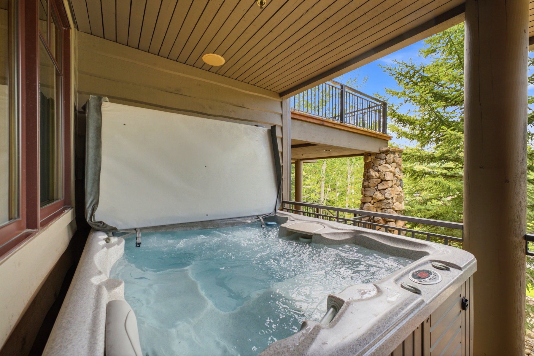 Outdoor hot tub with an open cover under a covered balcony