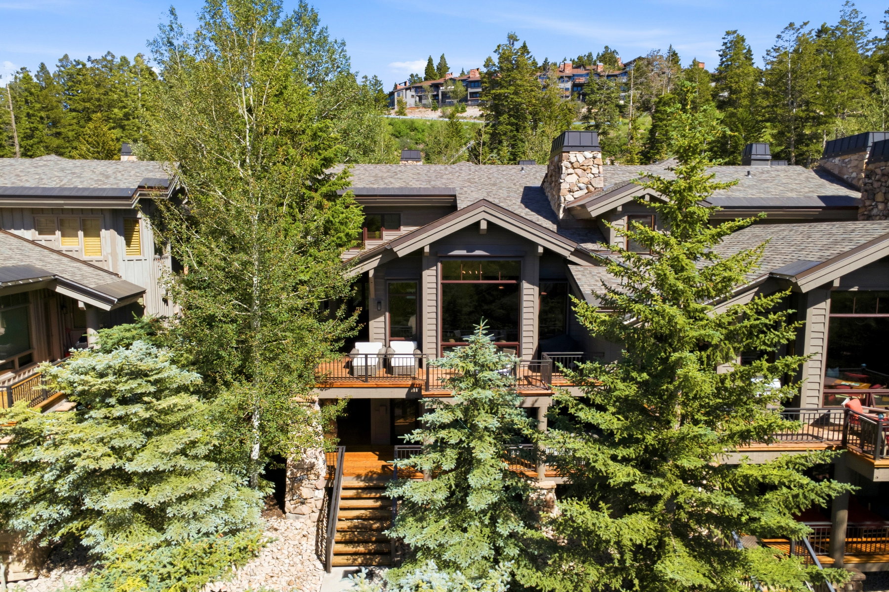 Multi-level property featuring dark wood siding, multiple decks with dark railings, and a stone chimney