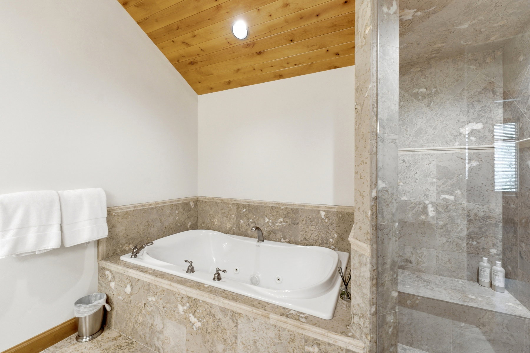 Soaking tub with a tiled surround, complemented by a wood-paneled ceiling and recessed lighting