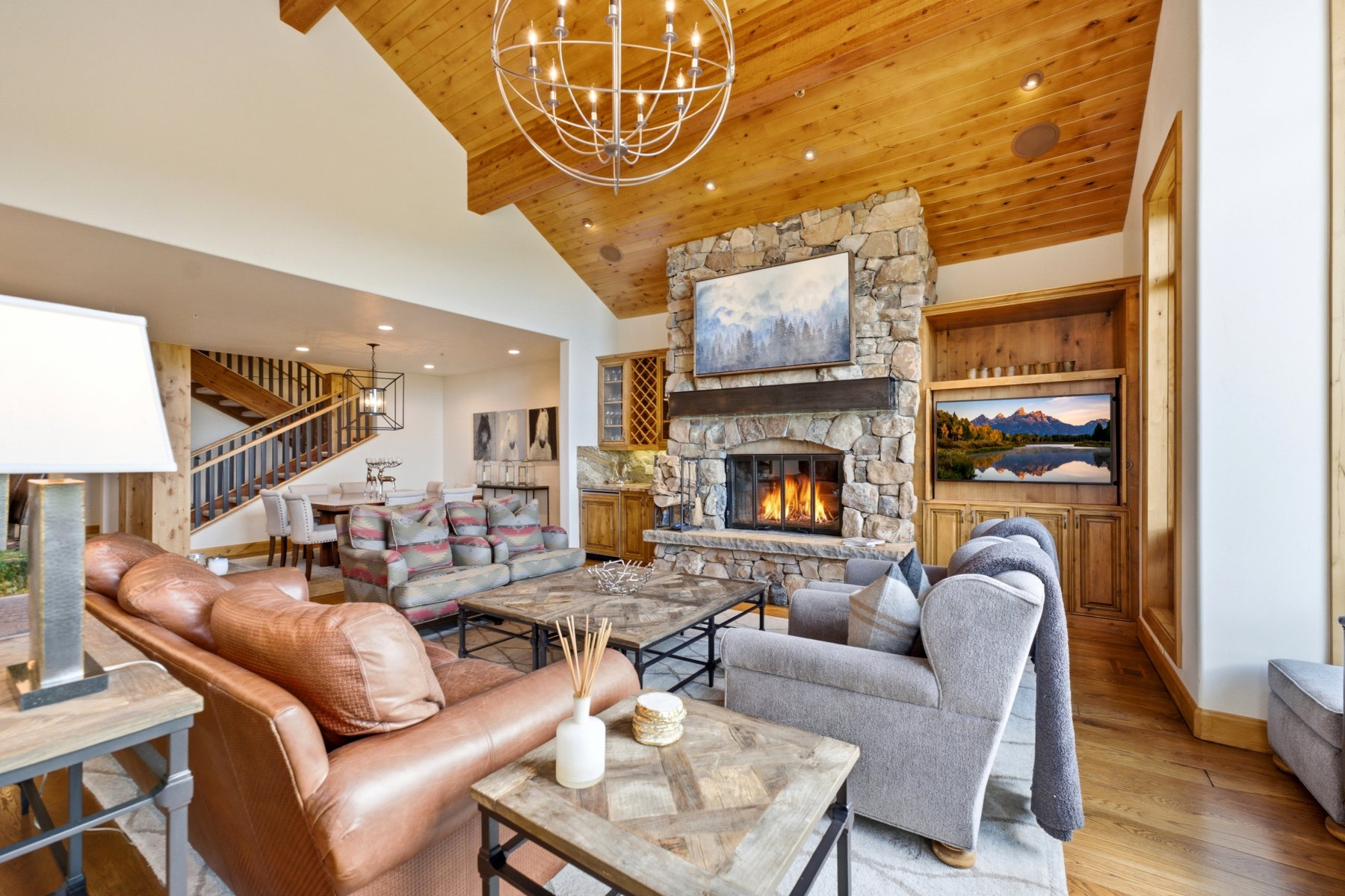Living area featuring a stone fireplace with a wood mantle, custom built-in cabinetry, wood-finish flooring, and a vaulted wood-paneled ceiling with an overhead chandelier