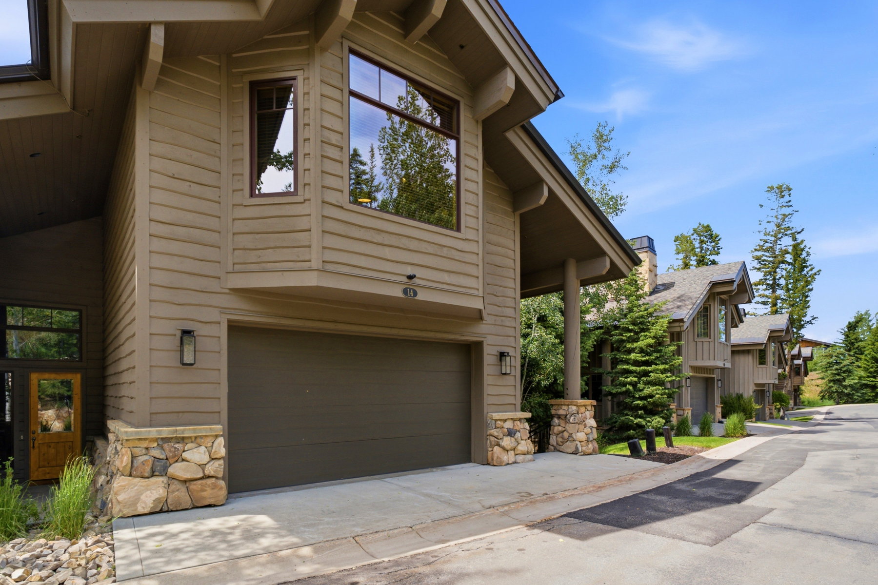 Exterior showcasing natural wood siding, a prominent two-car garage, and stone accent pillars