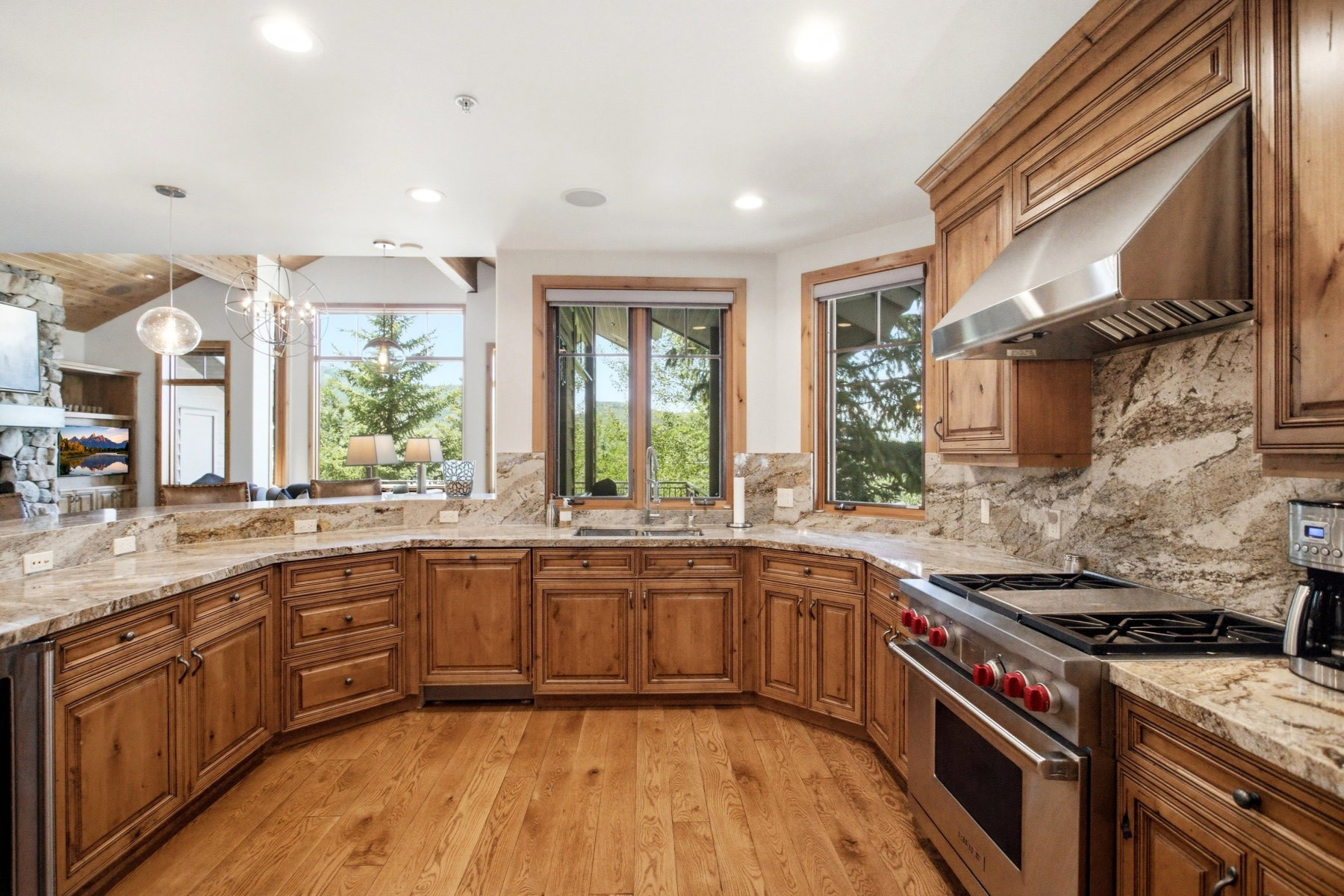 Spacious kitchen featuring expansive wood-finish flooring, custom wood cabinetry, and granite countertops with a matching backsplash