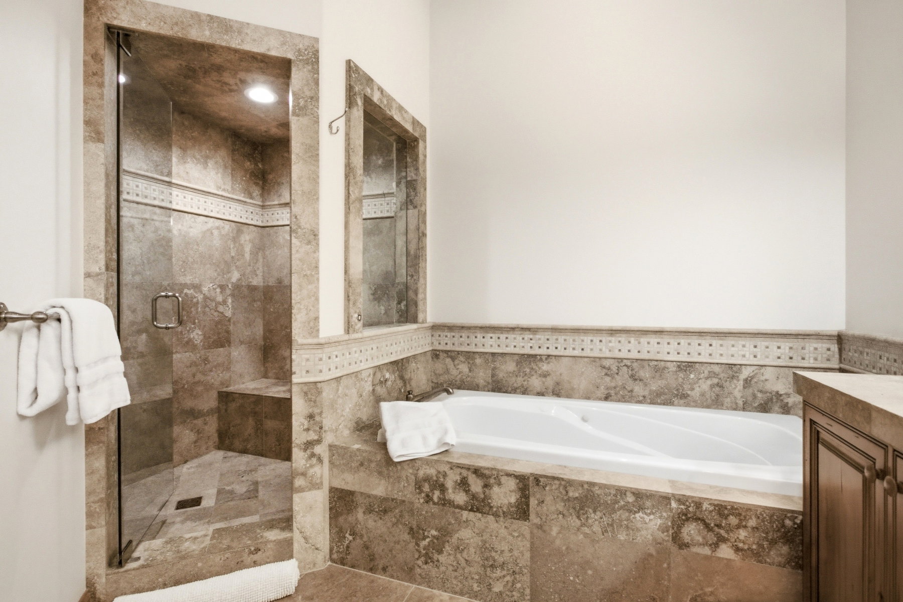 Tiled bathroom featuring a glass-enclosed shower with an integrated bench, a built-in soaking tub, and a vanity with an integrated countertop