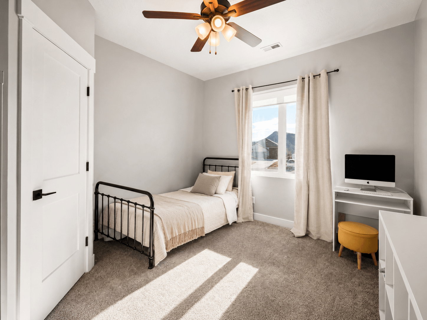 Carpeted room with a ceiling fan, a window with curtains, and a white door featuring matte black hardware