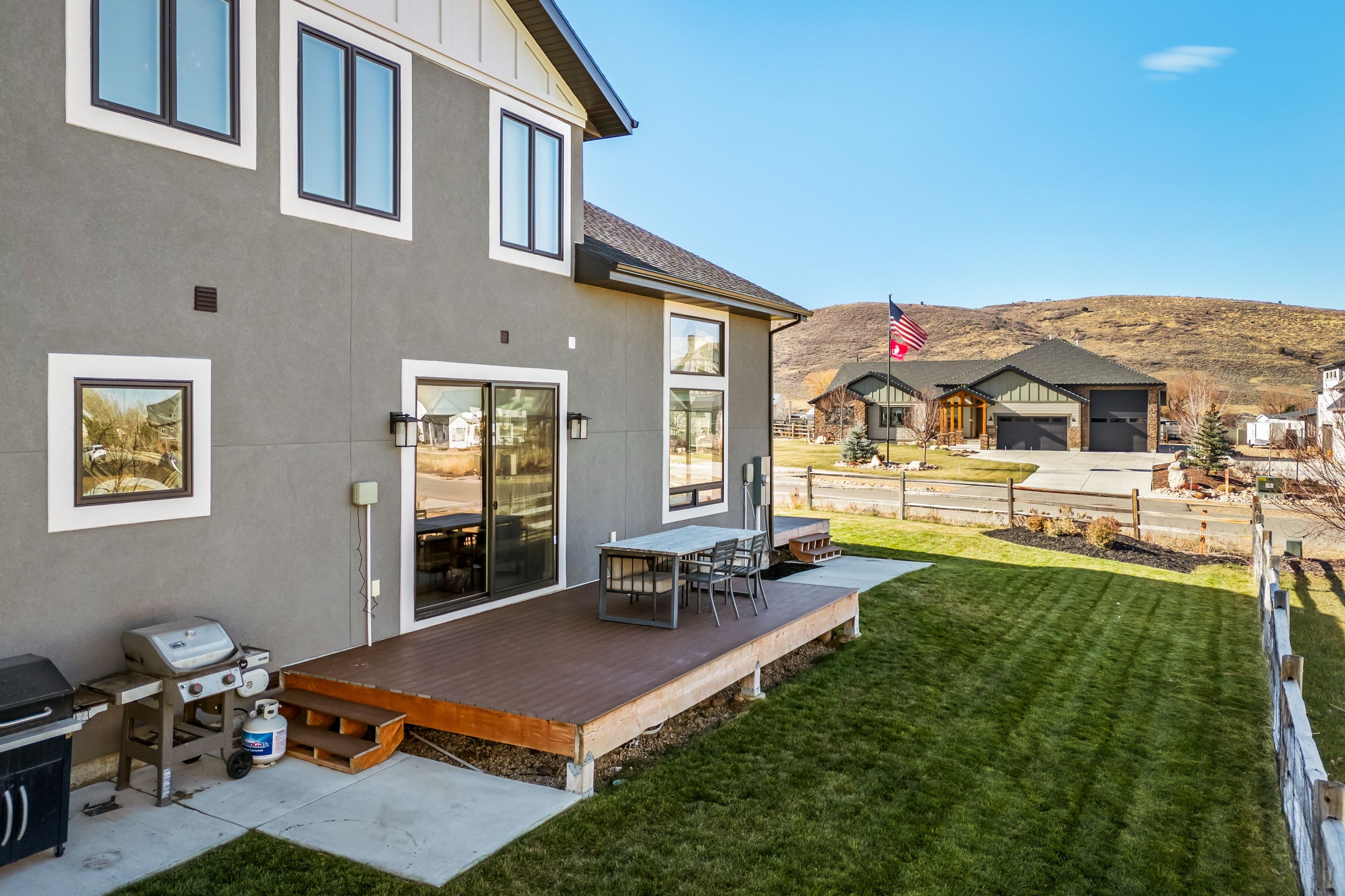 Rear exterior featuring a large elevated deck with steps to the lawn, sliding glass doors, and contemporary exterior lighting
