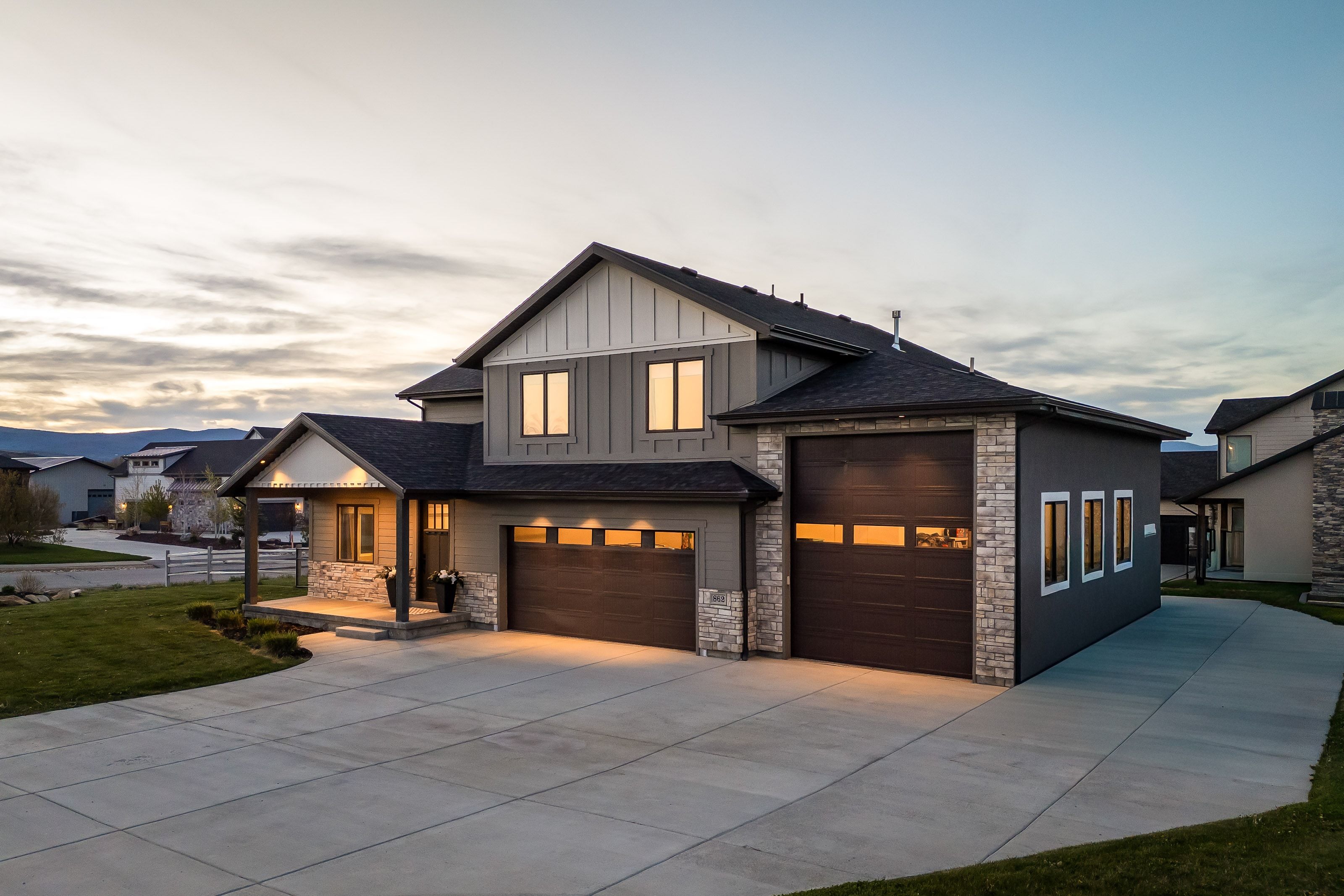 Modern exterior featuring vertical and horizontal siding, stone accents, multiple garage doors, a covered porch entry, and a concrete driveway