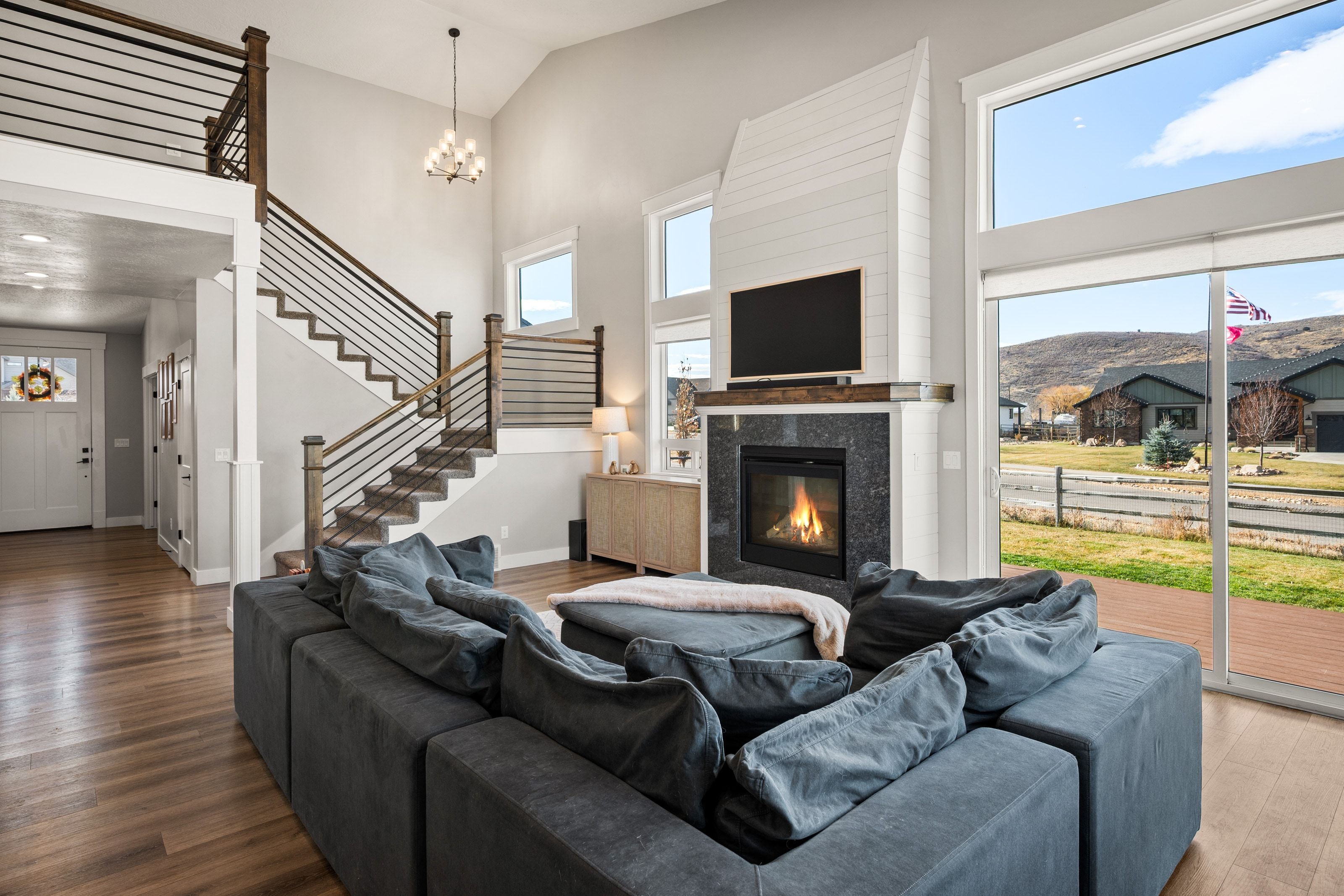 Vaulted living area featuring wood-finish flooring, a contemporary fireplace with dark stone surround, and tall windows with a sliding glass door
