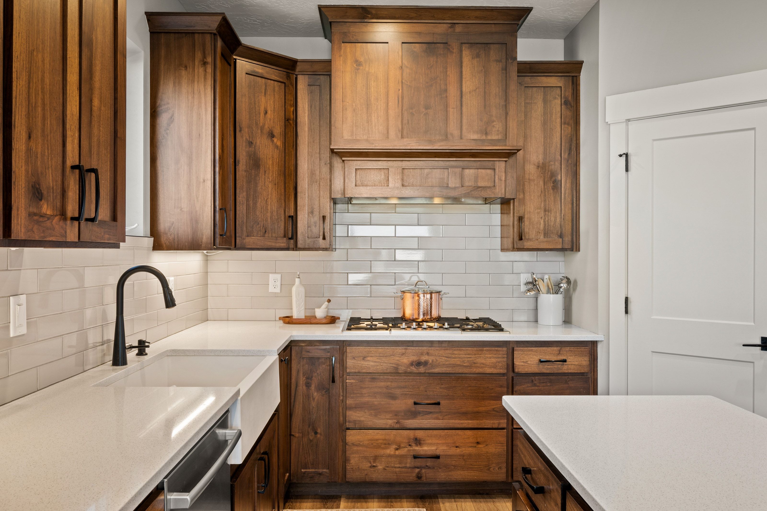 Kitchen featuring rich wood cabinetry, light countertops, a white subway tile backsplash, and a farmhouse-style sink with a matte black faucet