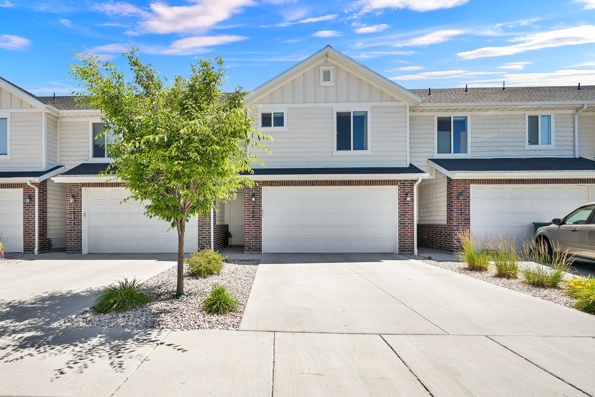 Modern townhome exterior featuring light-colored siding, dark shingles, brick accents, and a two-car garage