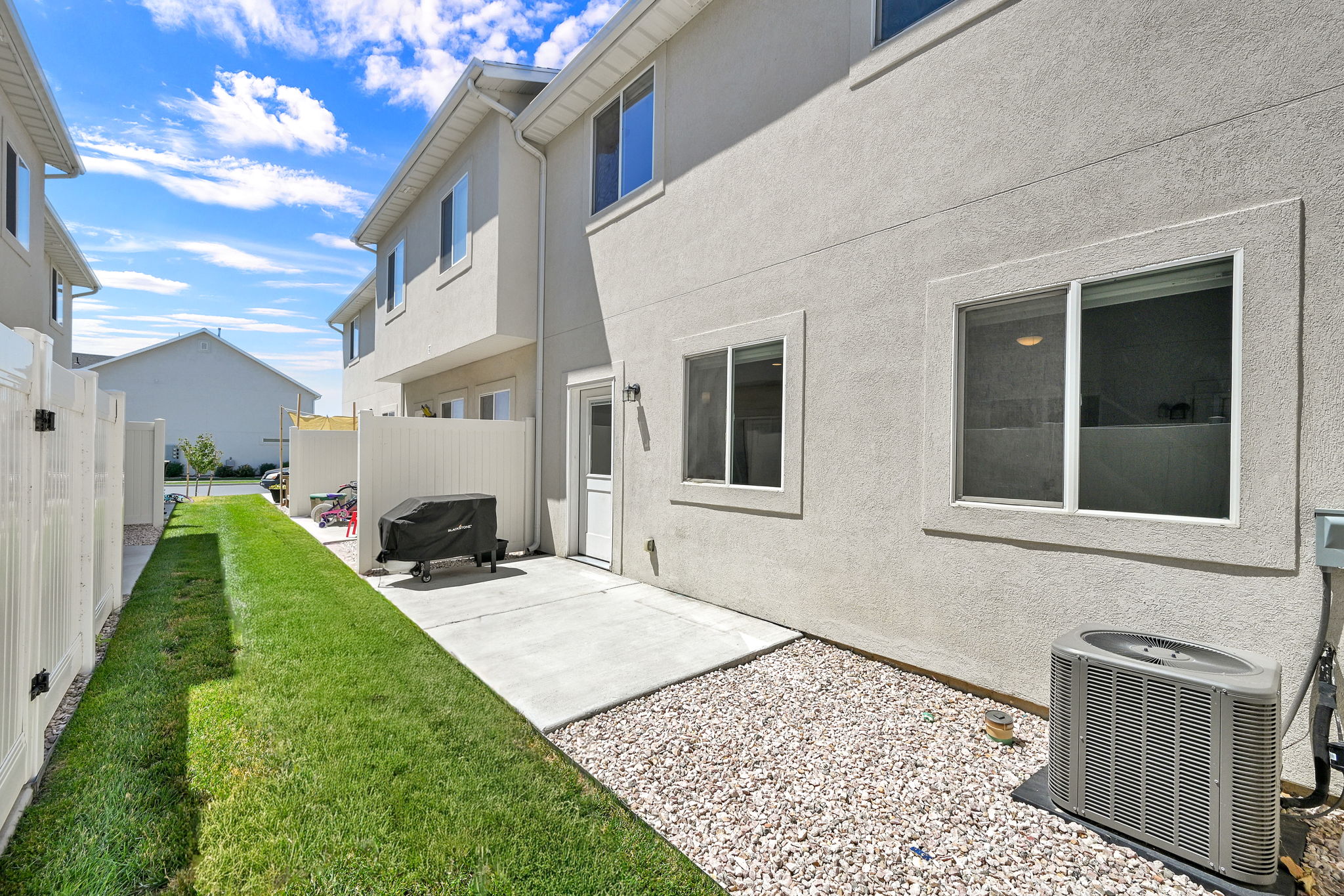 Rear exterior featuring stucco siding, multiple windows, a private concrete patio, and a gravel area