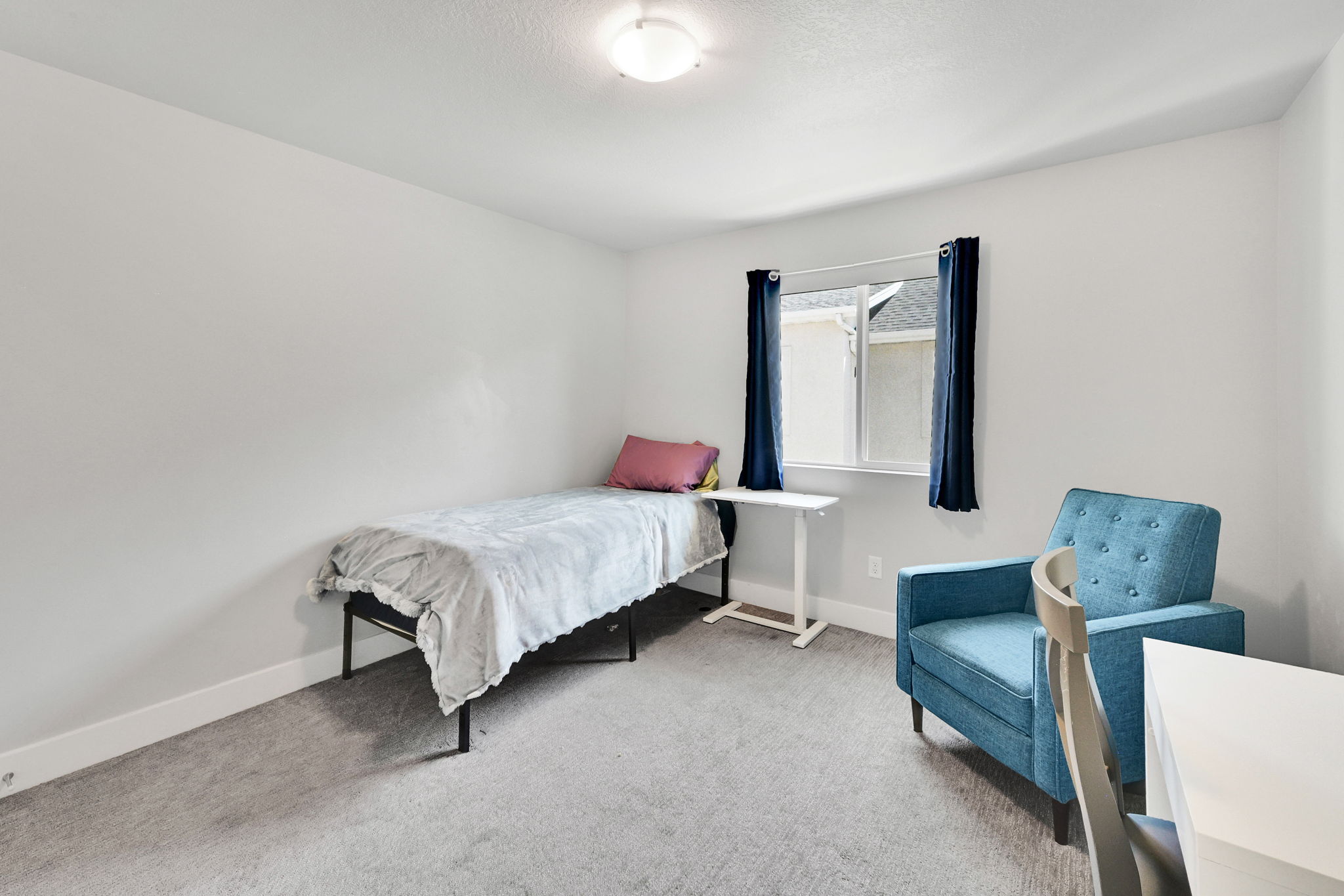 Neutral toned walls with a window featuring dark curtains, overhead lighting, and carpet flooring