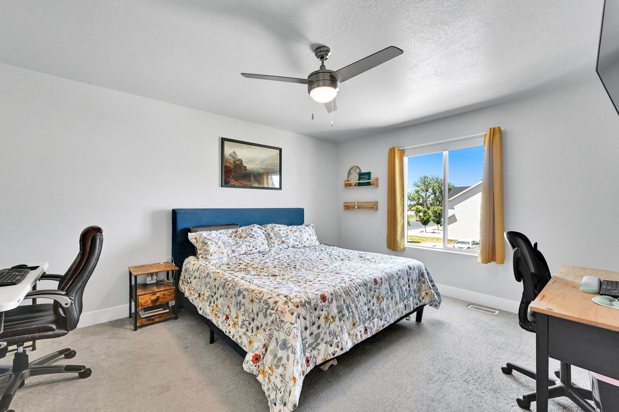 Bedroom featuring light gray carpeting, a large window with yellow drapes, and a ceiling fan with integrated lighting
