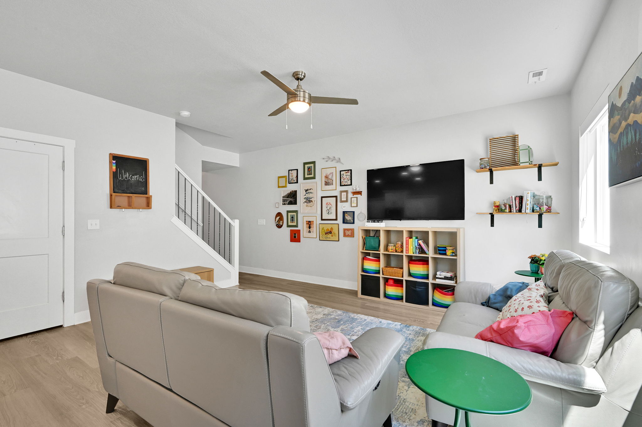 Bright living area featuring wood-finish flooring, a contemporary ceiling fan with integrated lighting, a built-in shelving unit, and a window providing natural light