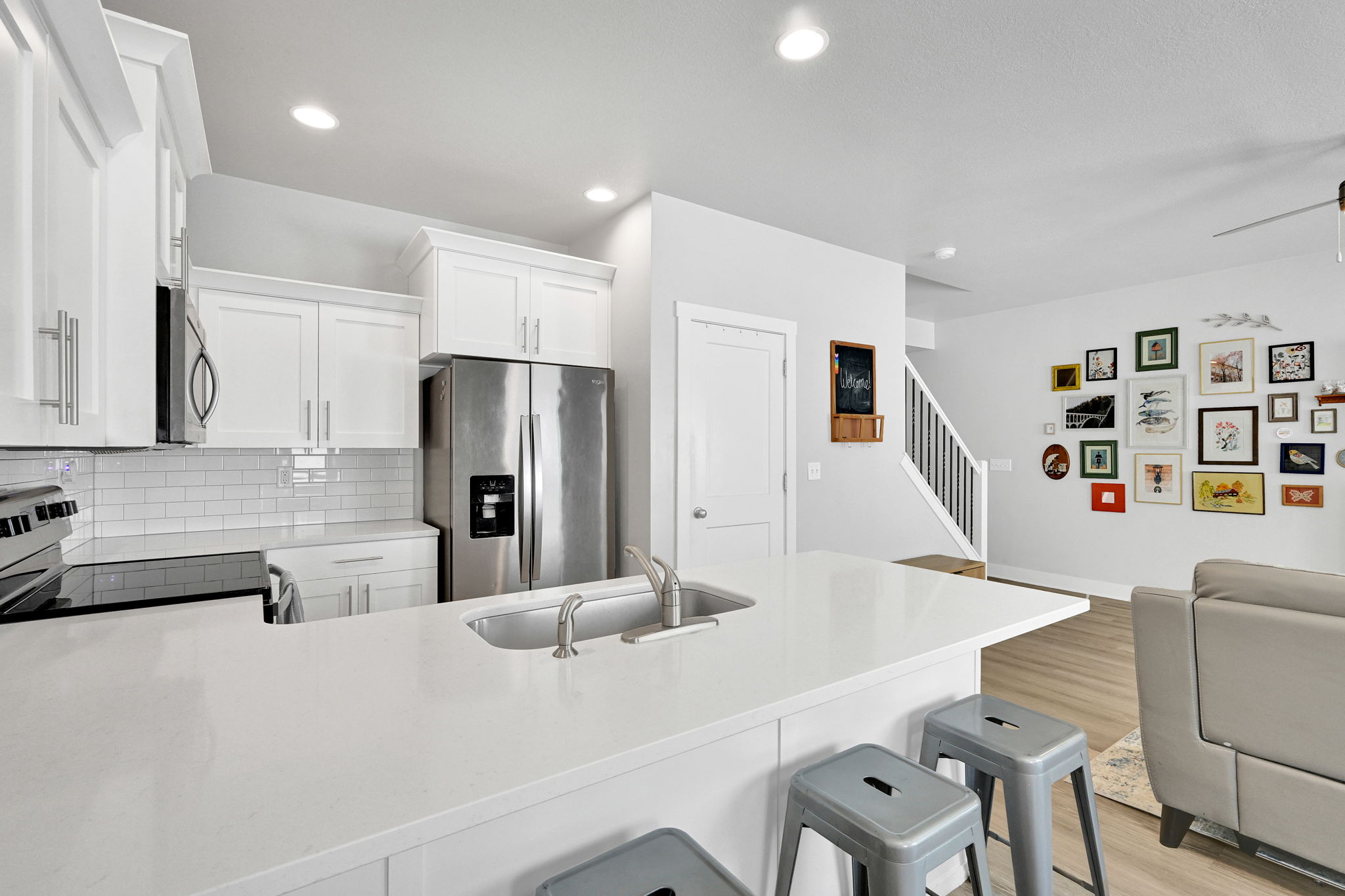 Modern kitchen featuring a large island with an undermount sink, white shaker cabinetry, stainless steel appliances, white subway tile backsplash, and recessed lighting