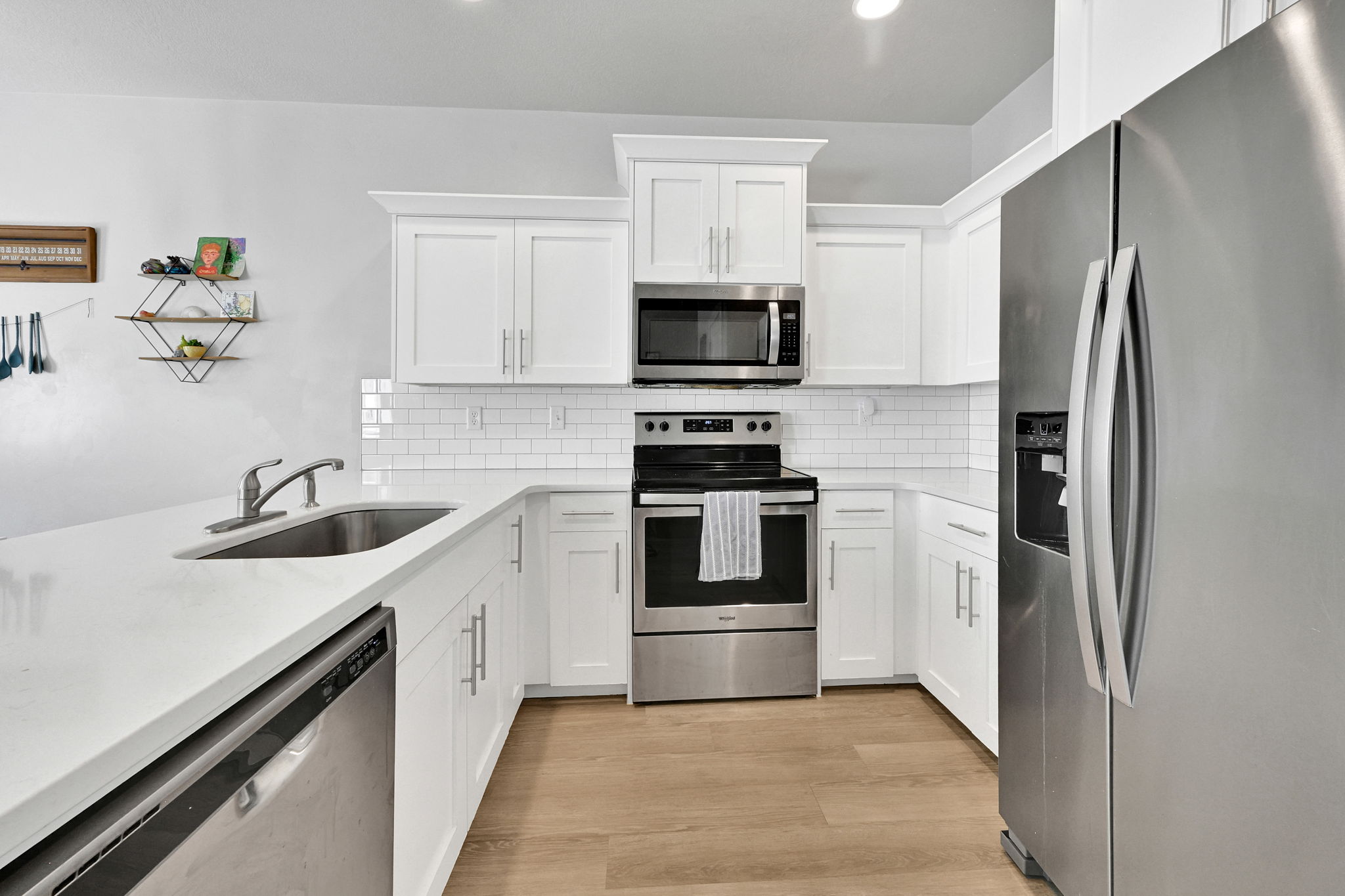 Modern kitchen featuring white shaker cabinetry, stainless steel appliances, a subway tile backsplash, and light wood-finish flooring