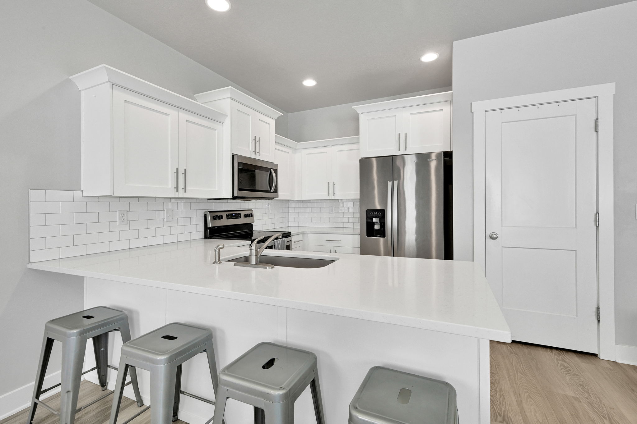 Kitchen featuring white shaker cabinetry, stainless steel appliances, a subway tile backsplash, and a large central island with a sink