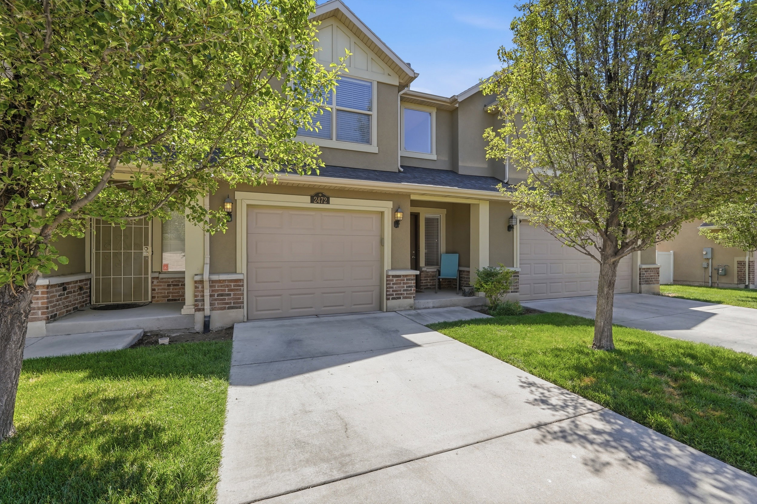 Two-story stucco and brick exterior featuring a single-car garage with an overhead door, covered front porch, and a concrete driveway
