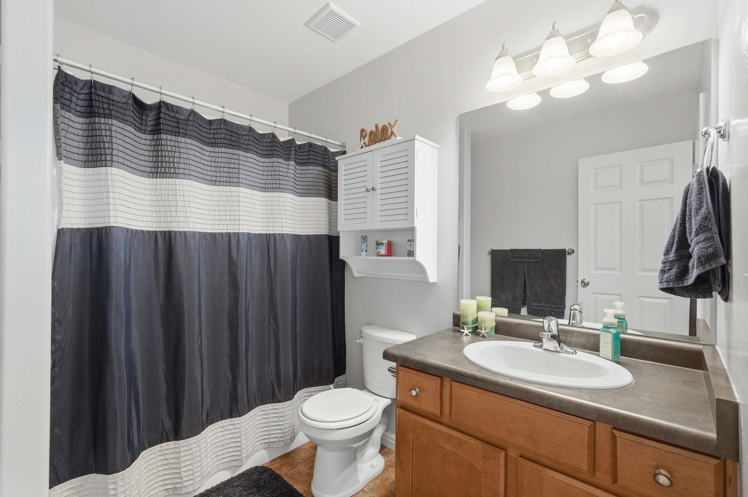 Bathroom featuring a wood-finish vanity with an integrated sink, a large wall mirror, and overhead vanity lighting