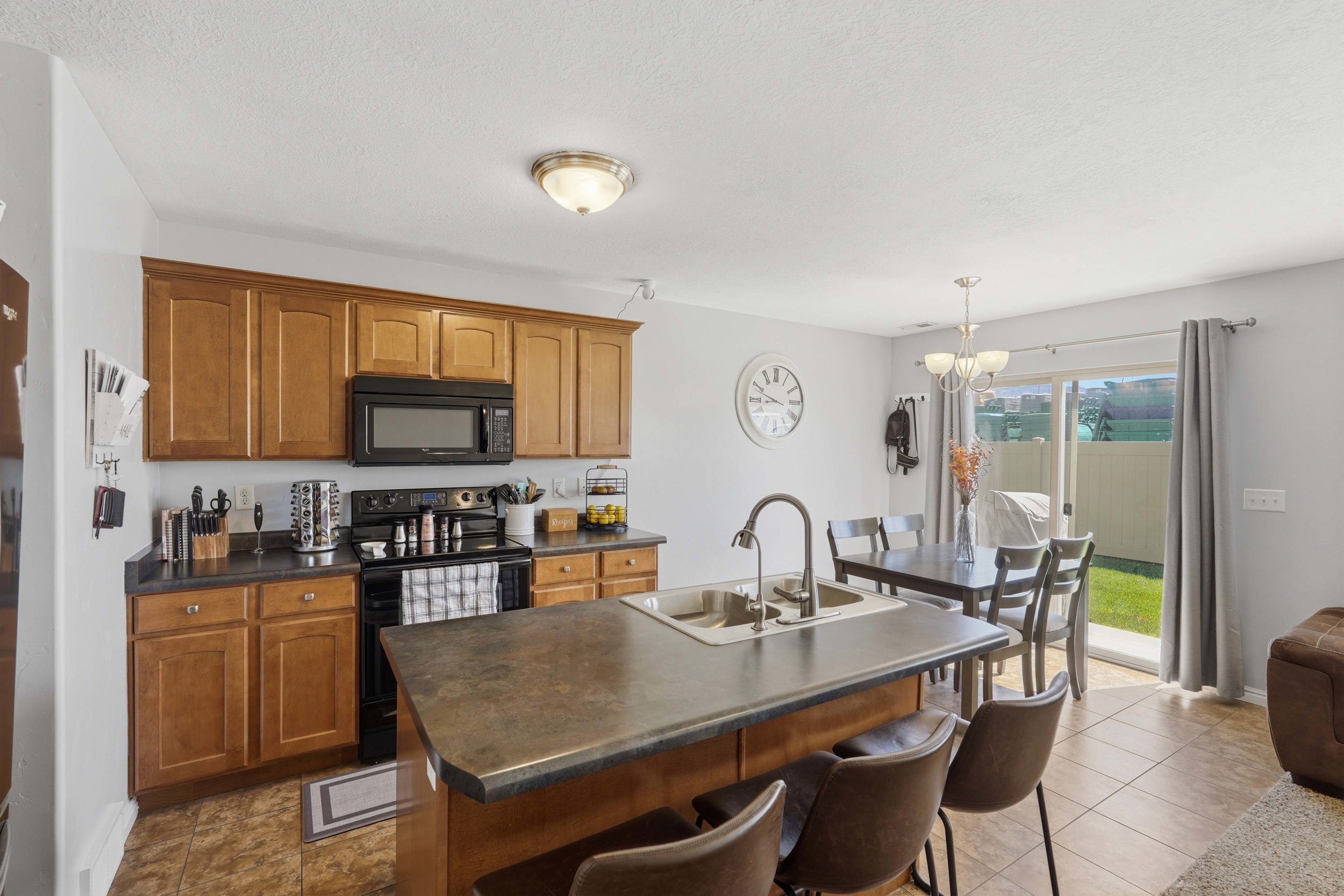 Kitchen featuring light wood-finish cabinetry, black appliances, and dark countertops