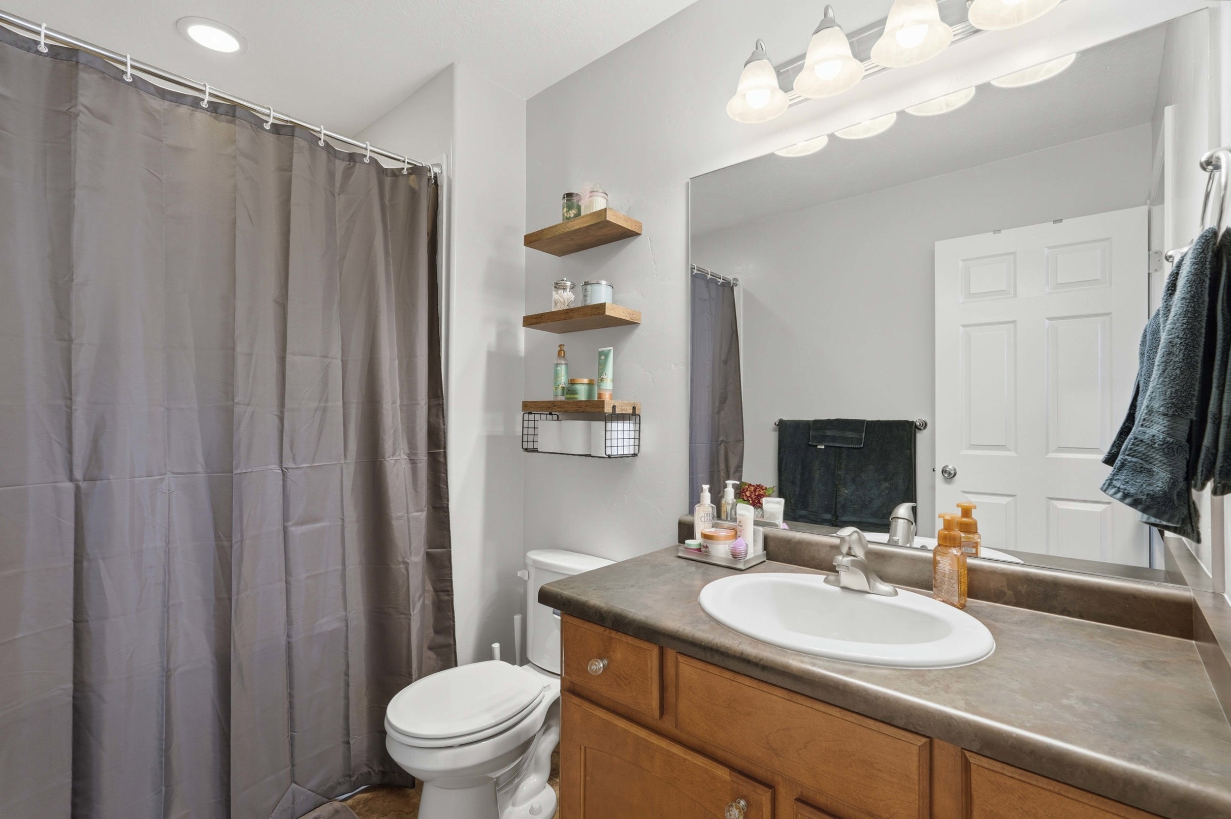 Bathroom featuring a wood-finish vanity with an integrated sink, a large wall-mounted mirror, and a five-light vanity fixture