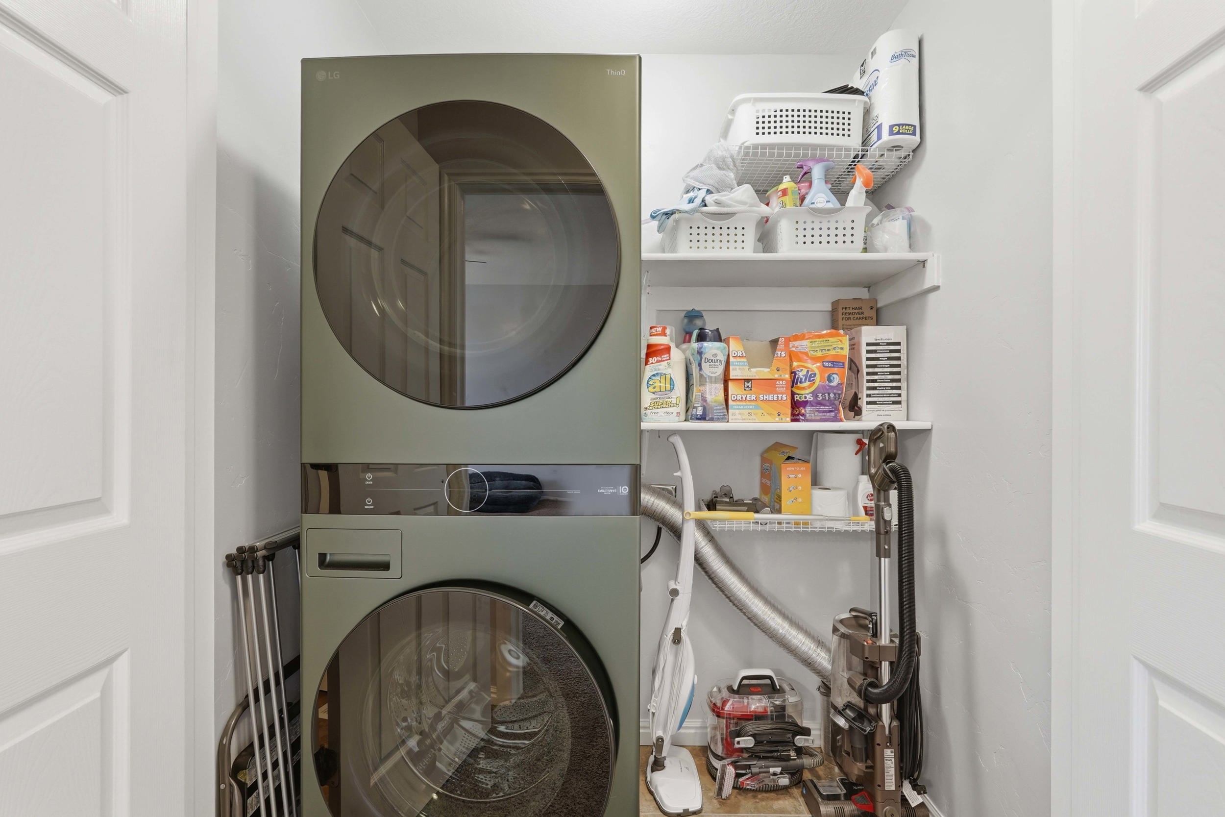 Dedicated laundry area featuring a stacked washer and dryer unit, integrated control panel, and white shelving for storage