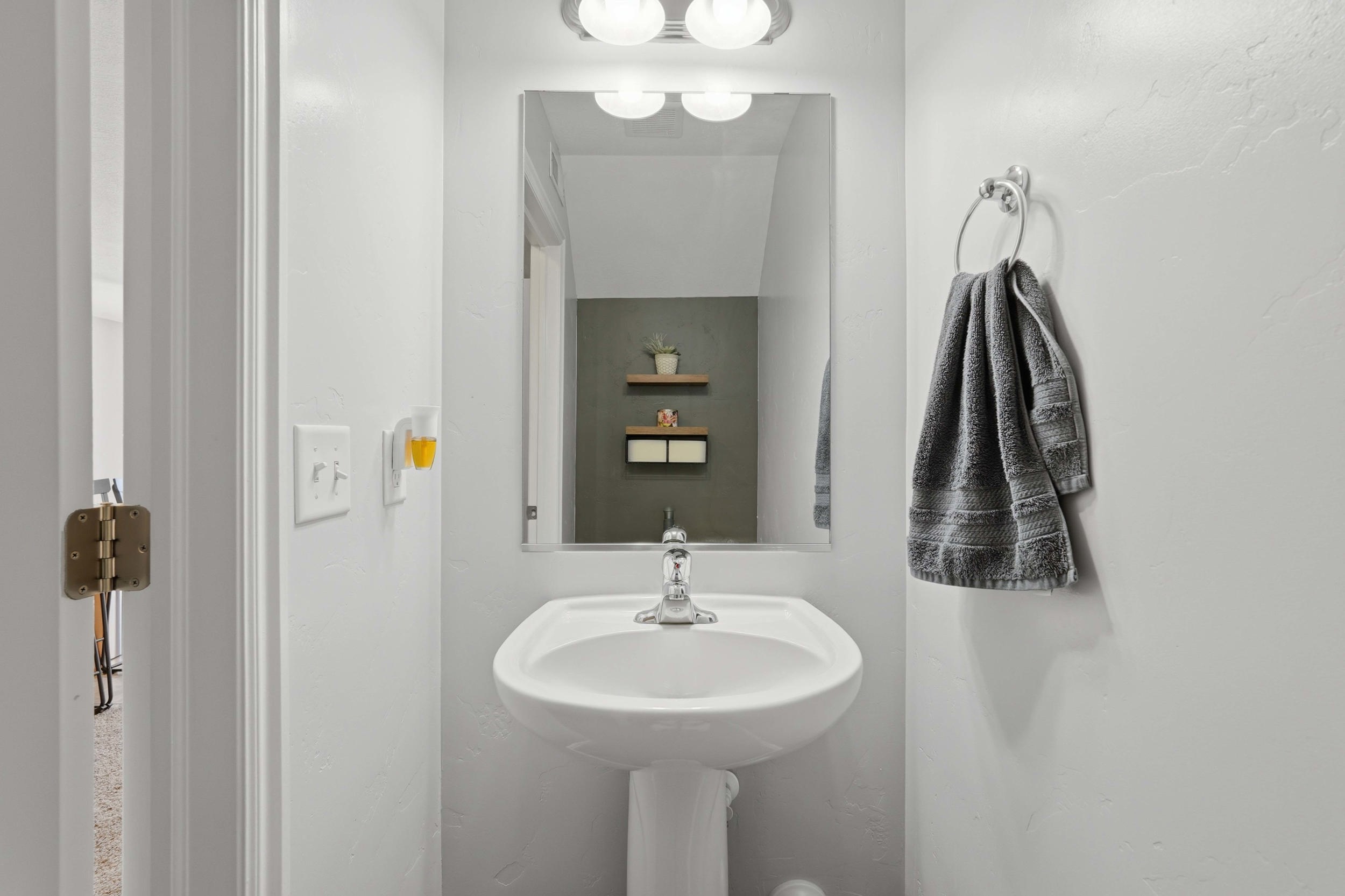 Pedestal sink with chrome faucet, framed mirror, and overhead vanity lighting
