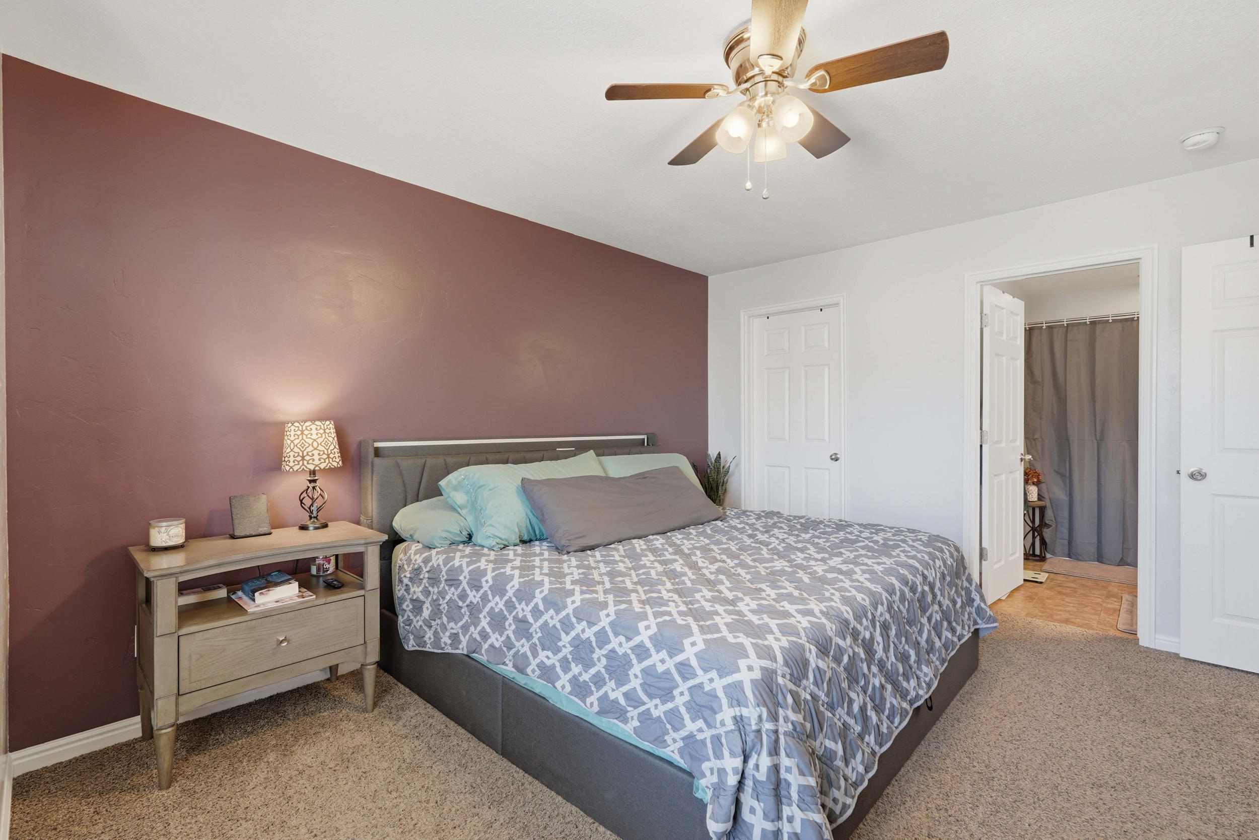Bedroom featuring a ceiling fan with integrated lighting, a plum accent wall, and neutral carpeting