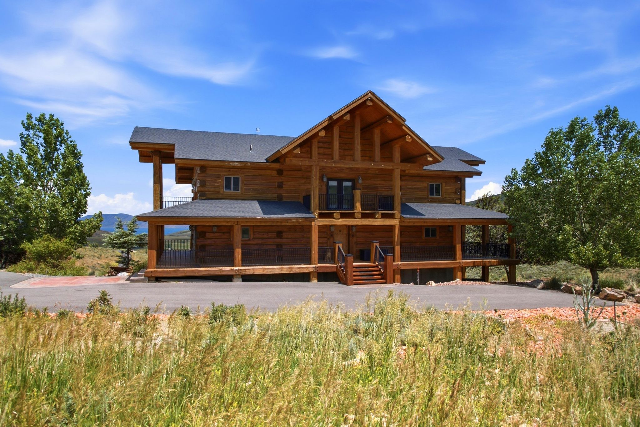 Custom log home featuring a covered front porch, an upper-level balcony, exposed log beams, a multi-pitch roofline, and a paved driveway