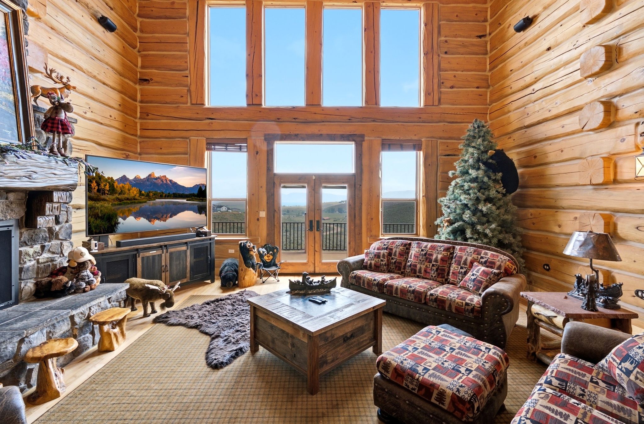 Spacious living area featuring log construction, a stone-clad fireplace with hearth, and double French doors to an outdoor area