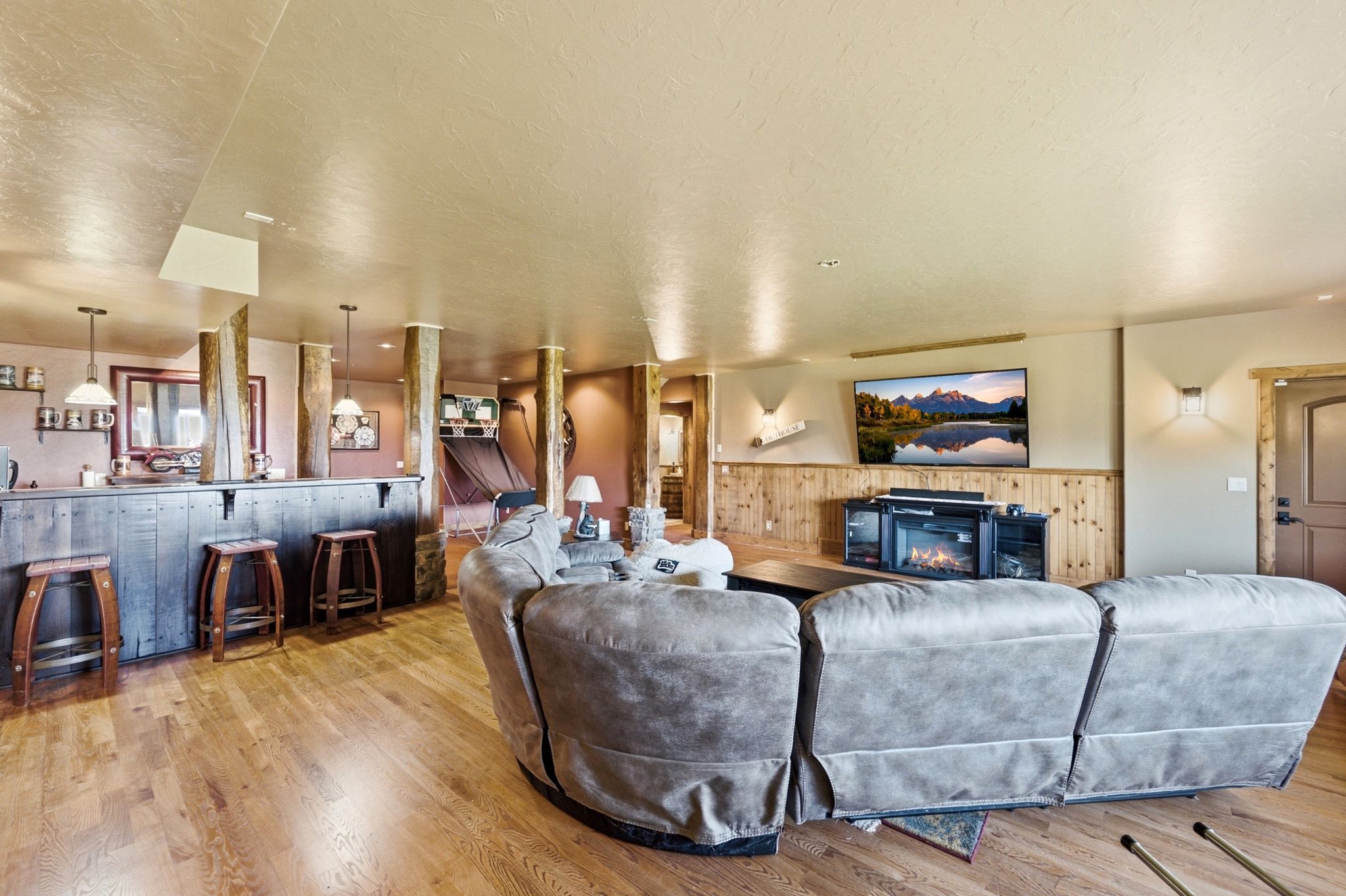 Entertainment room featuring wood-finish flooring, a built-in wet bar with pendant lighting, a wall-mounted television, and a built-in electric fireplace