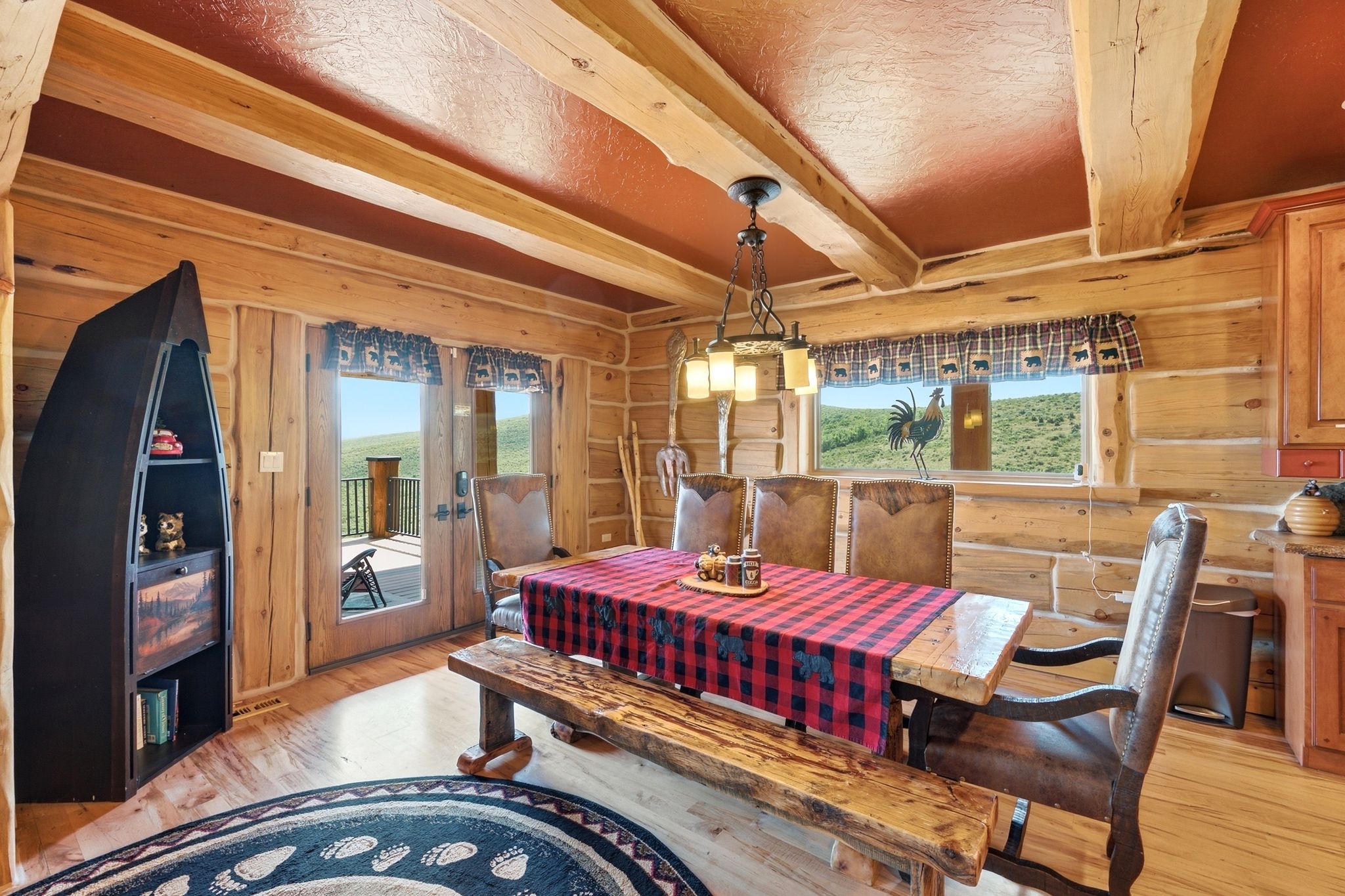 Dining area featuring log walls, exposed wood beams, wood-finish flooring, and a large window with distant scenery