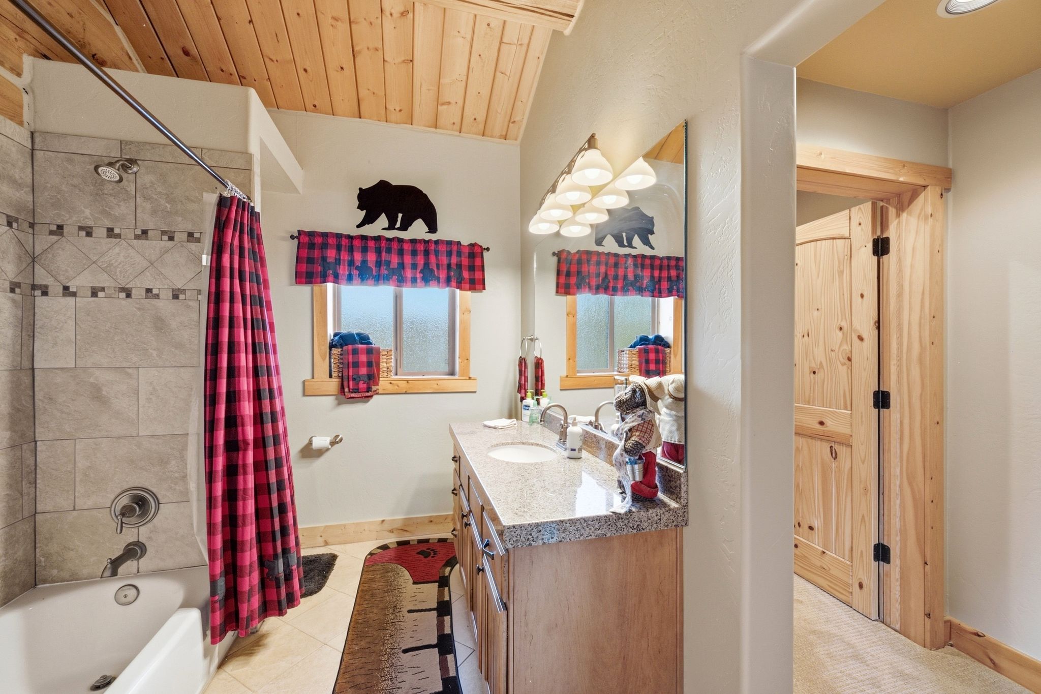 Bathroom featuring a wood-paneled ceiling, tiled tub/shower combination, light wood vanity with dual sinks, and light-colored countertop