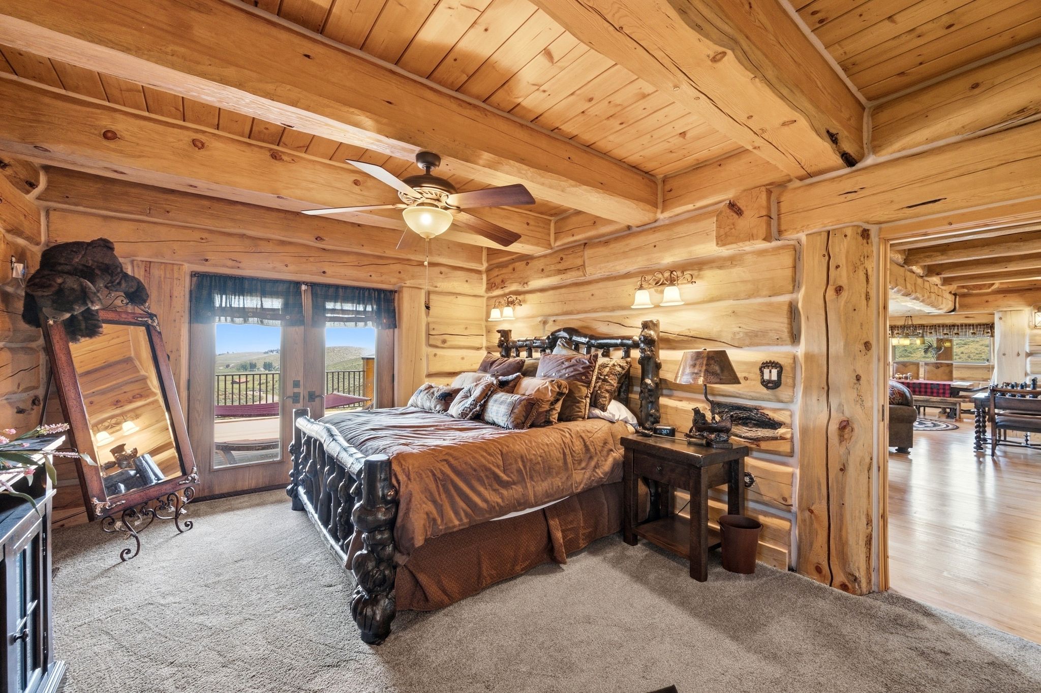 Rough-hewn log walls and exposed log beams define this room, featuring a double-door exterior entry with a balcony