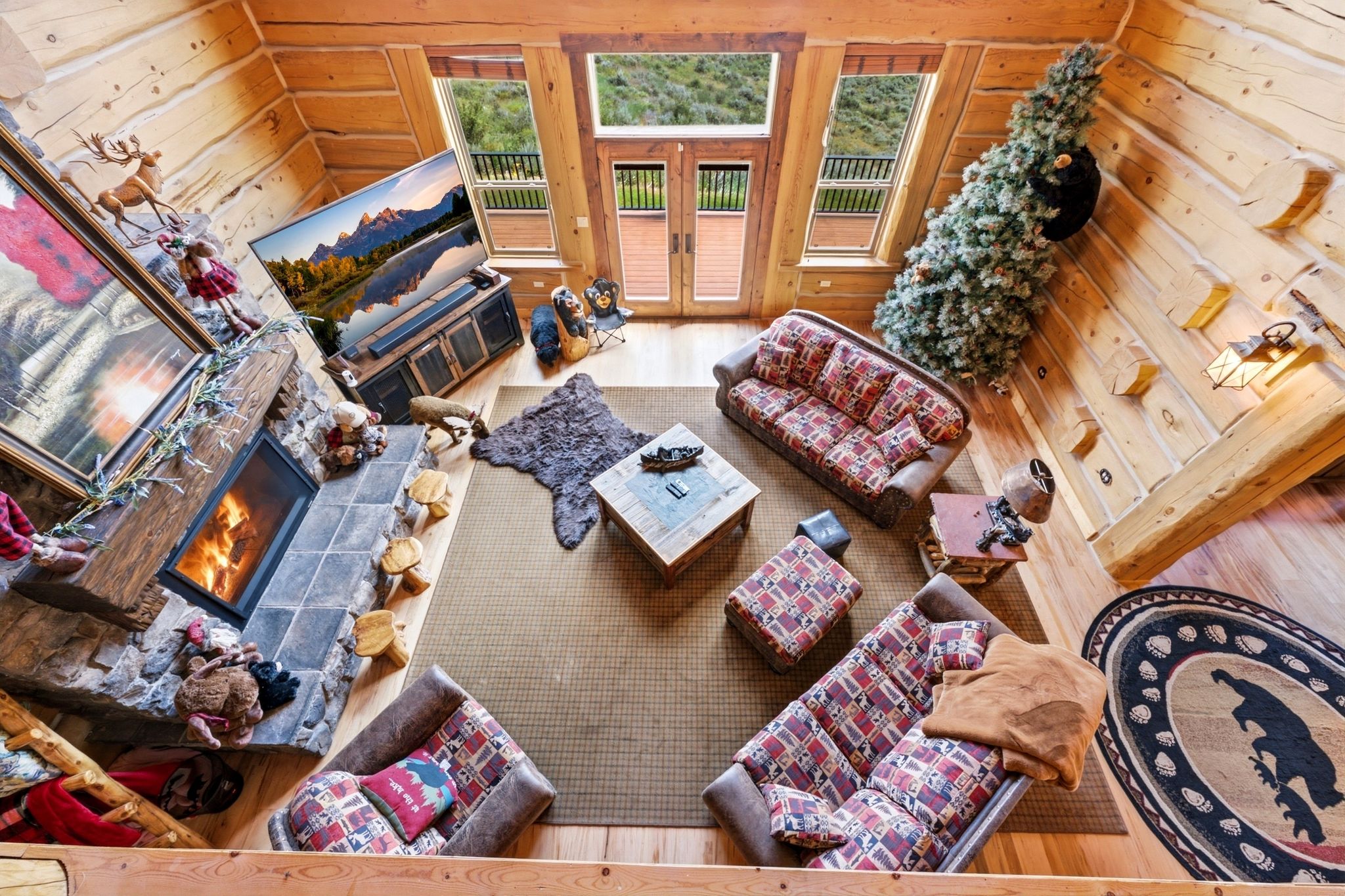 Spacious living area featuring exposed wood beam construction, a stone fireplace with a tiled hearth, wood-finish flooring, and multiple windows