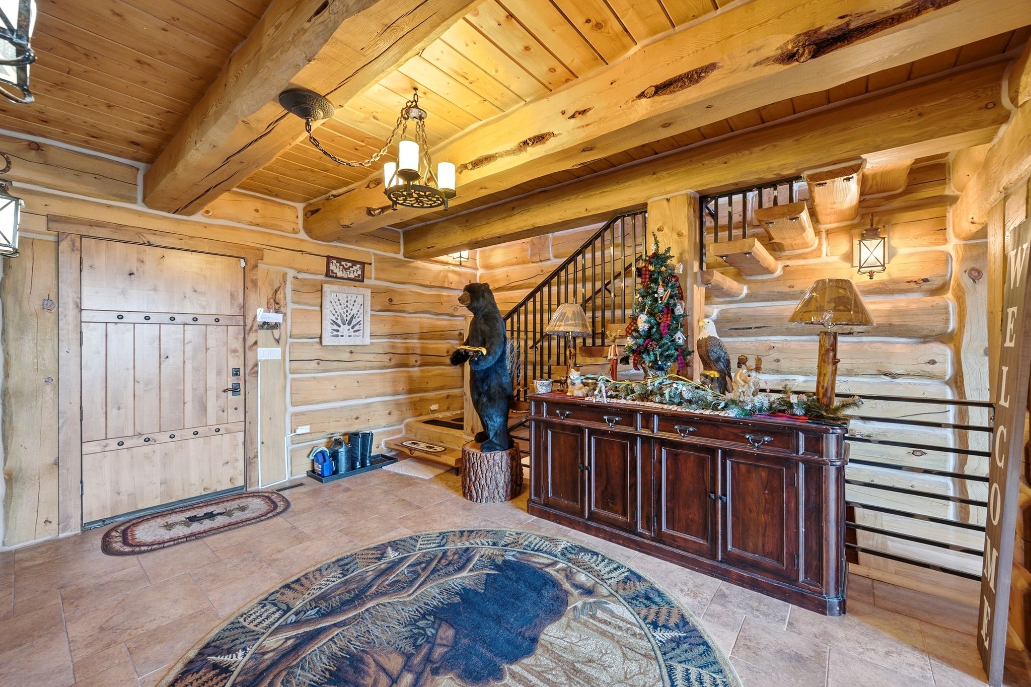 Expansive foyer featuring a solid wood entry door, natural wood-plank walls, exposed wood beams, a custom wood ceiling, and tile flooring