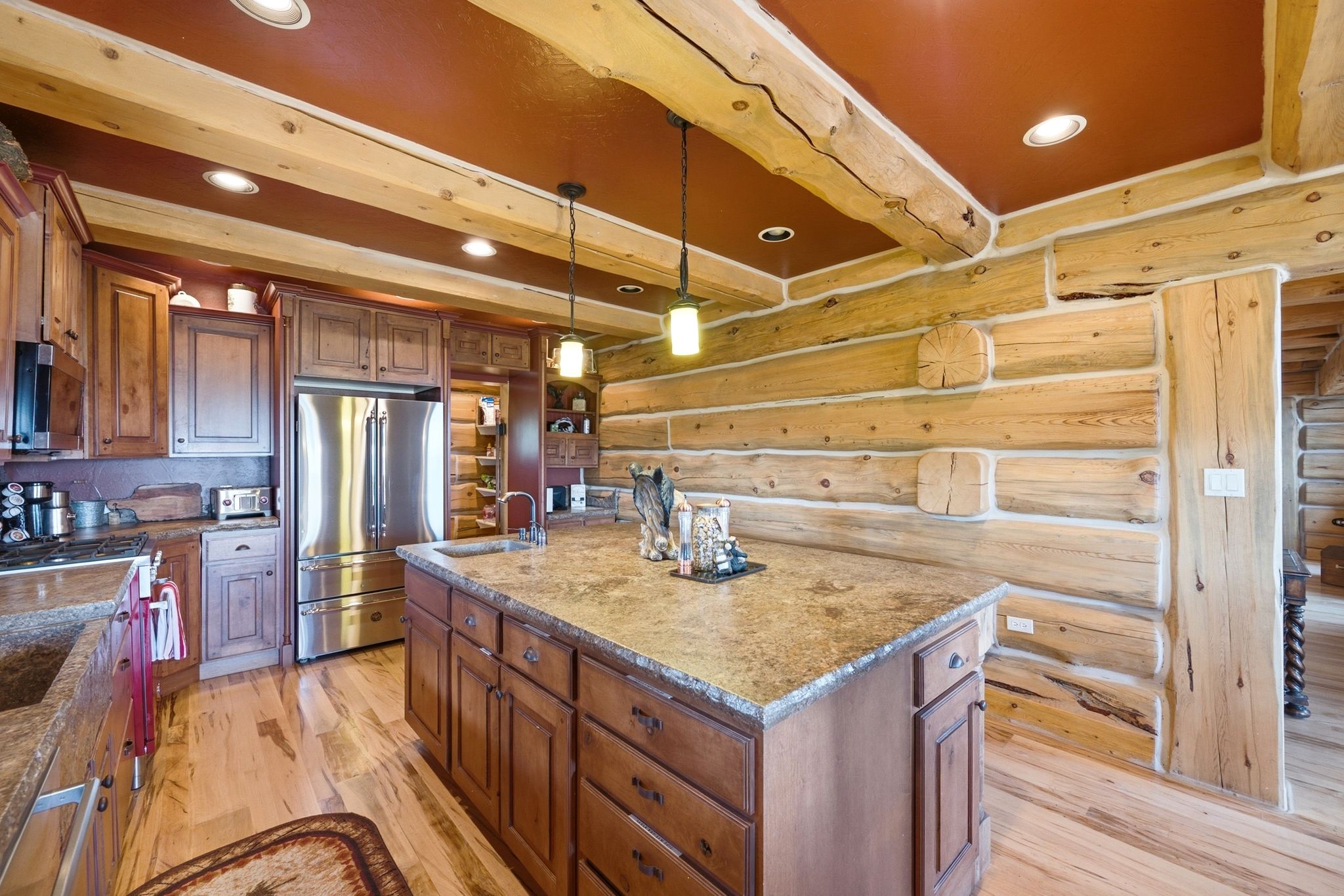 Rustic kitchen featuring log walls, an expansive center island with a stone-finish countertop, wood-finish flooring, and exposed wood beams