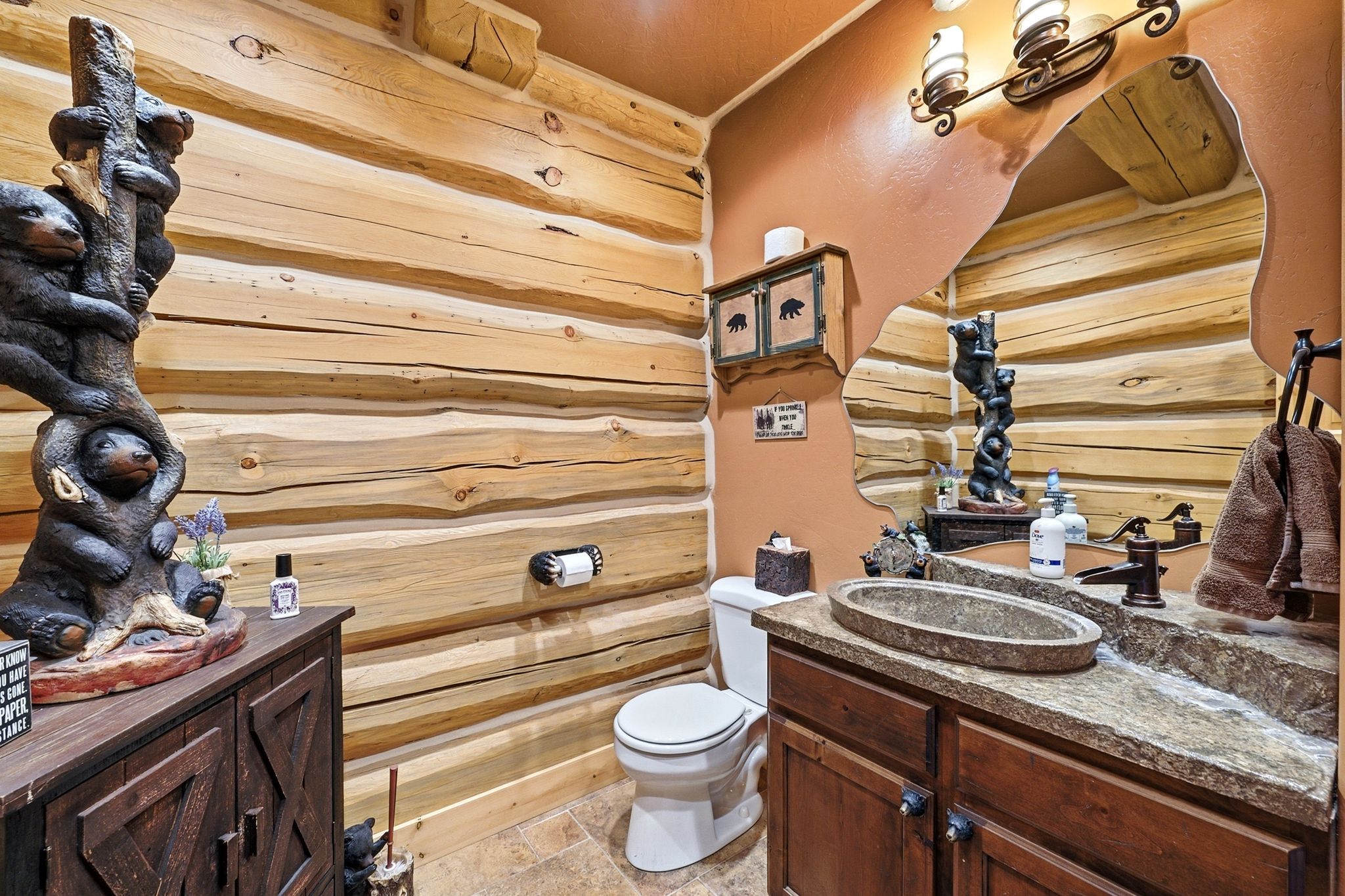 Bathroom featuring robust log-style wall paneling, a stone vessel sink set into a complementary stone-finish countertop, and a dark wood-finish vanity cabinet with double doors